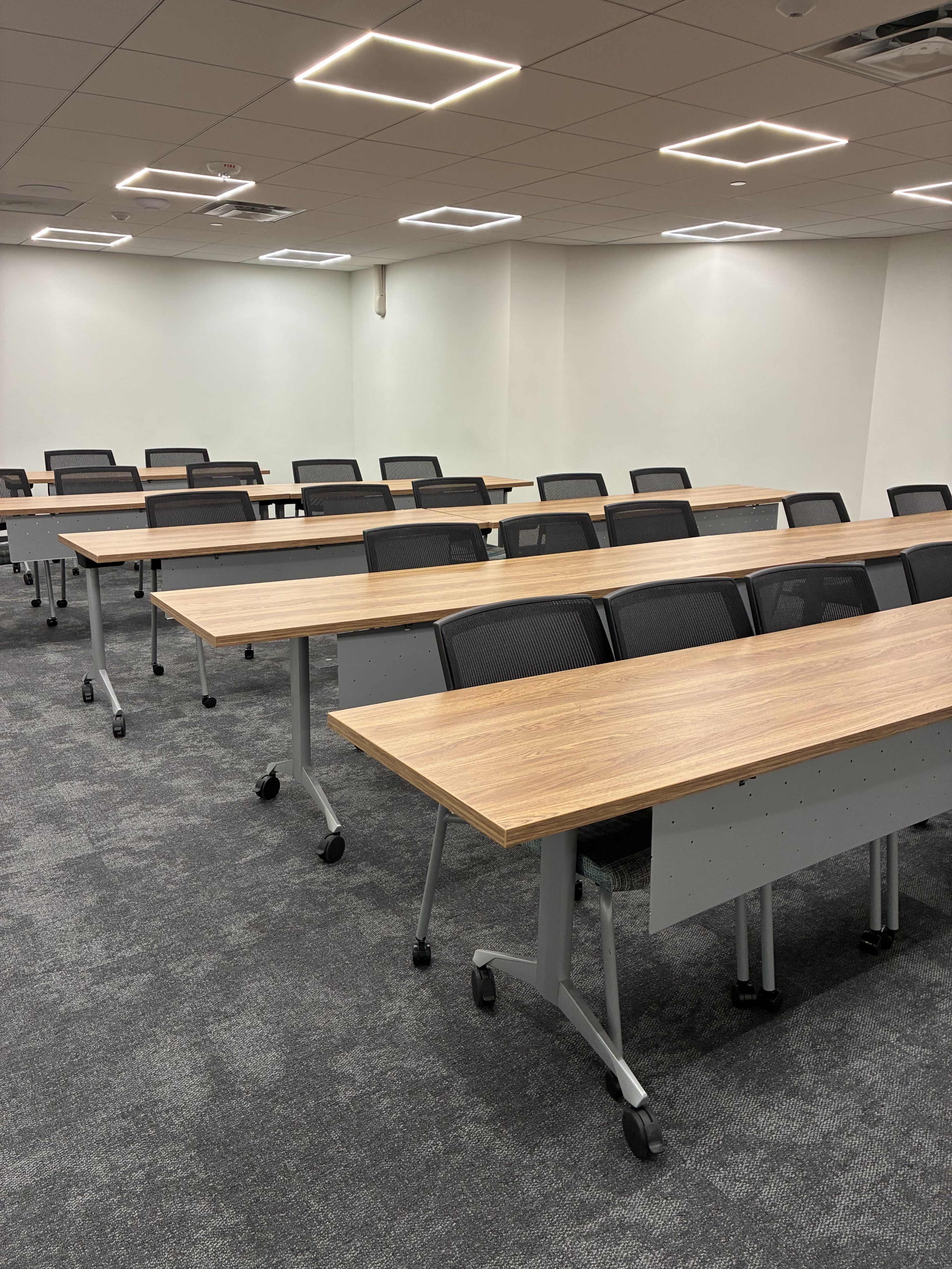 A well-lit conference room features multiple rows of tables and chairs arranged for a presentation or meeting.
