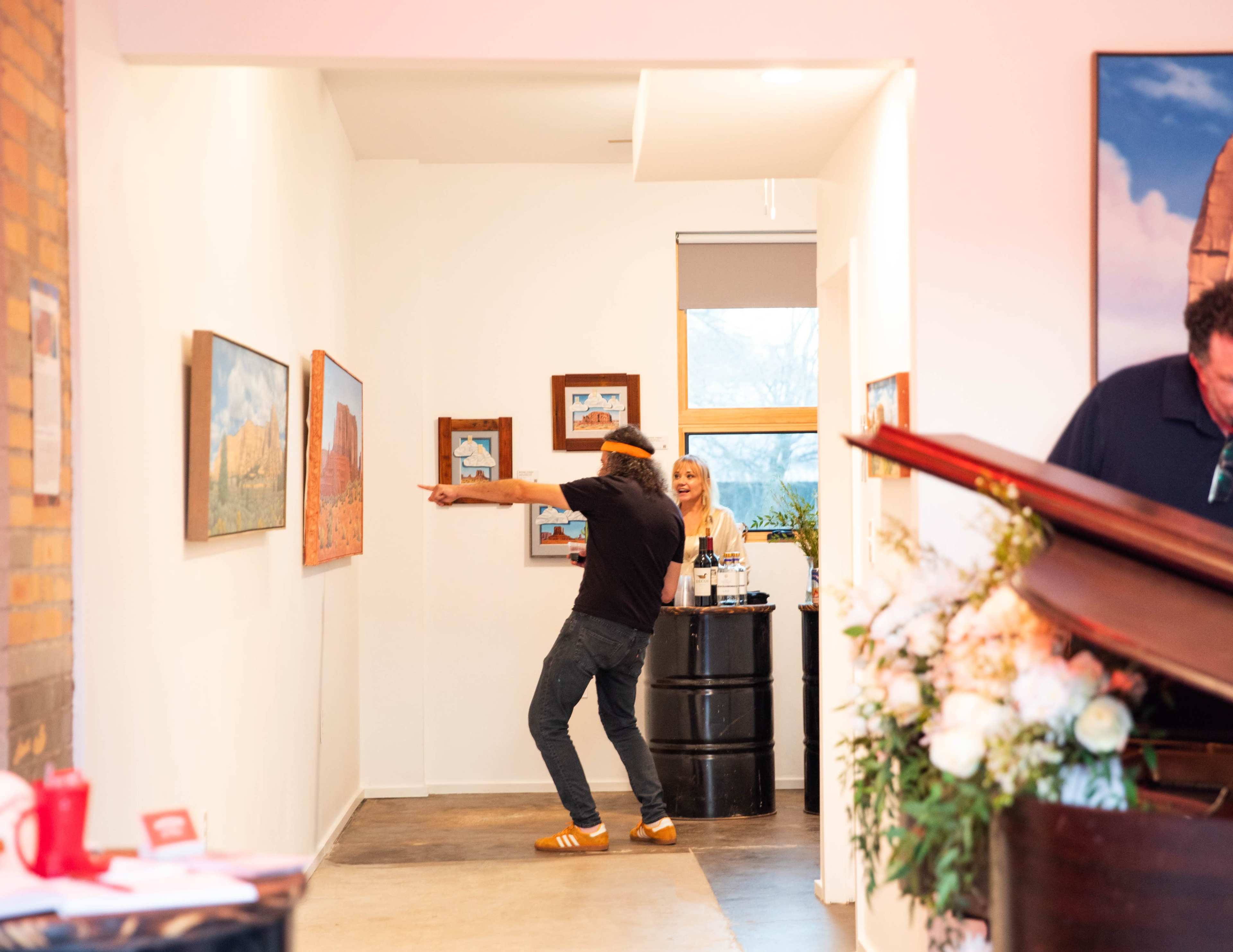 A person in casual attire dances animatedly in an art gallery while another person stands behind a bar counter, observing.