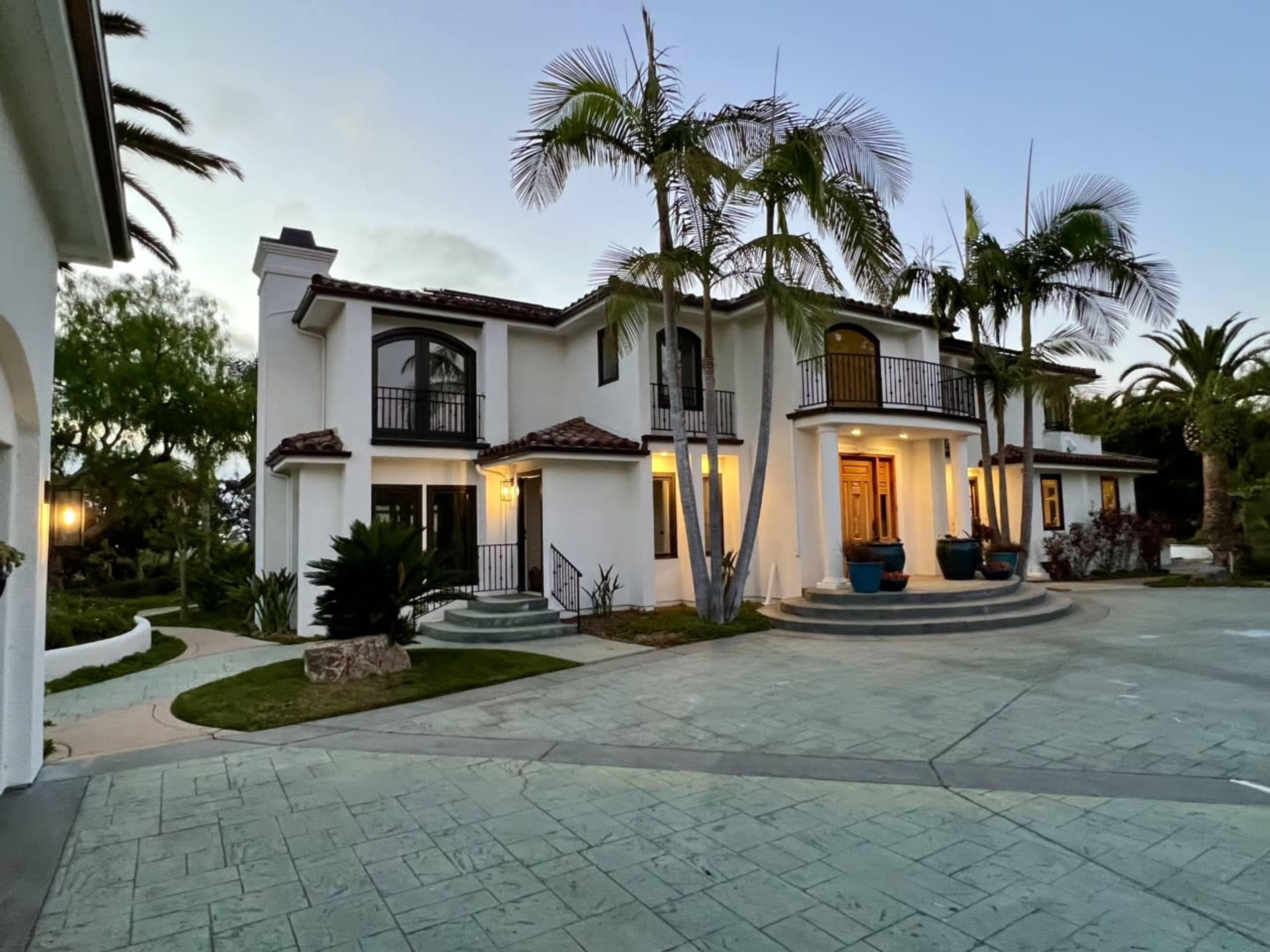 A two-story white house with a tiled roof, surrounded by palm trees and landscaped gardens.