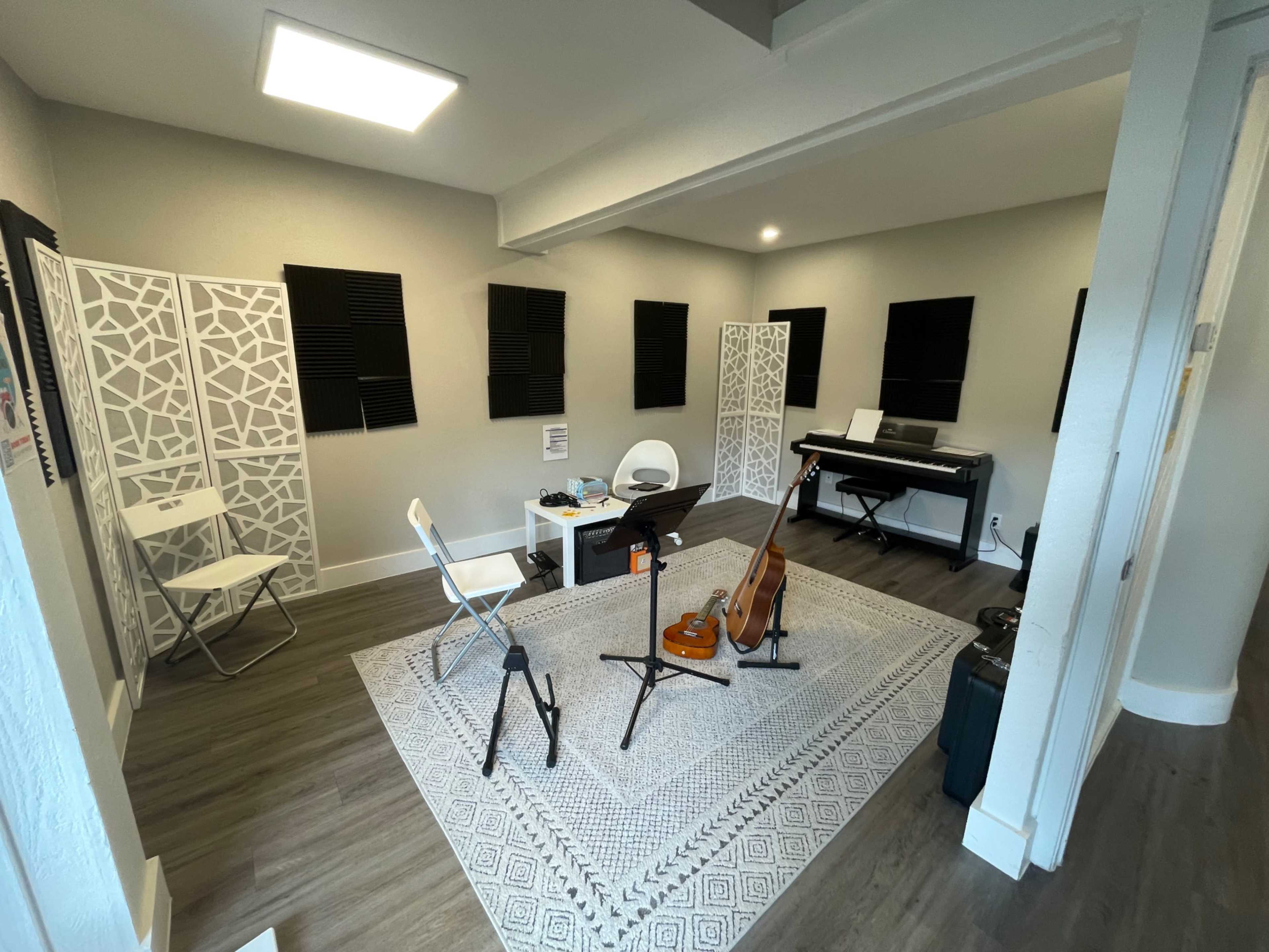 The image shows a music practice room with a rug, a piano, chairs, and music stands arranged neatly.