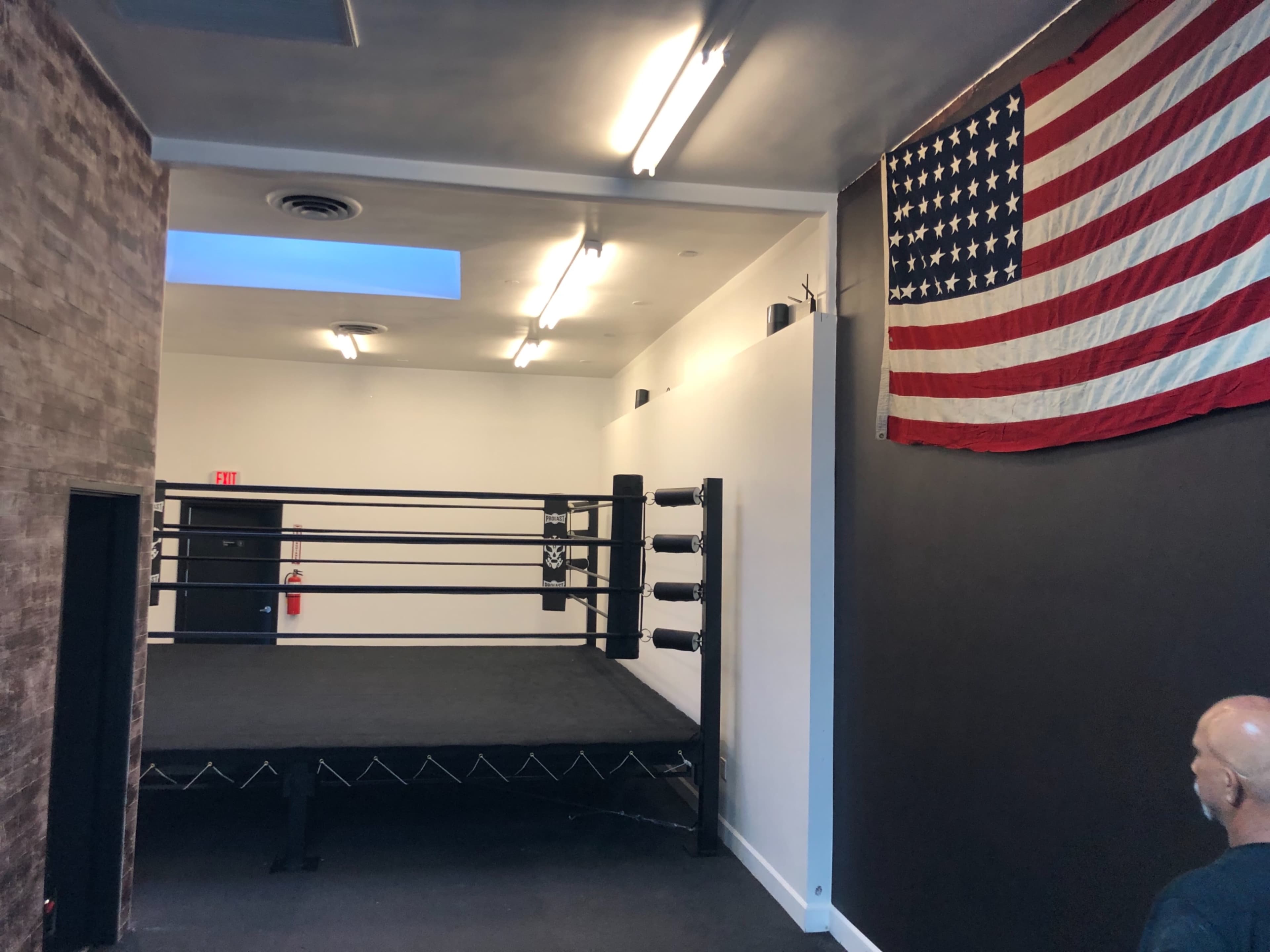A boxing ring set up in a minimalist room with an American flag mounted on the wall.