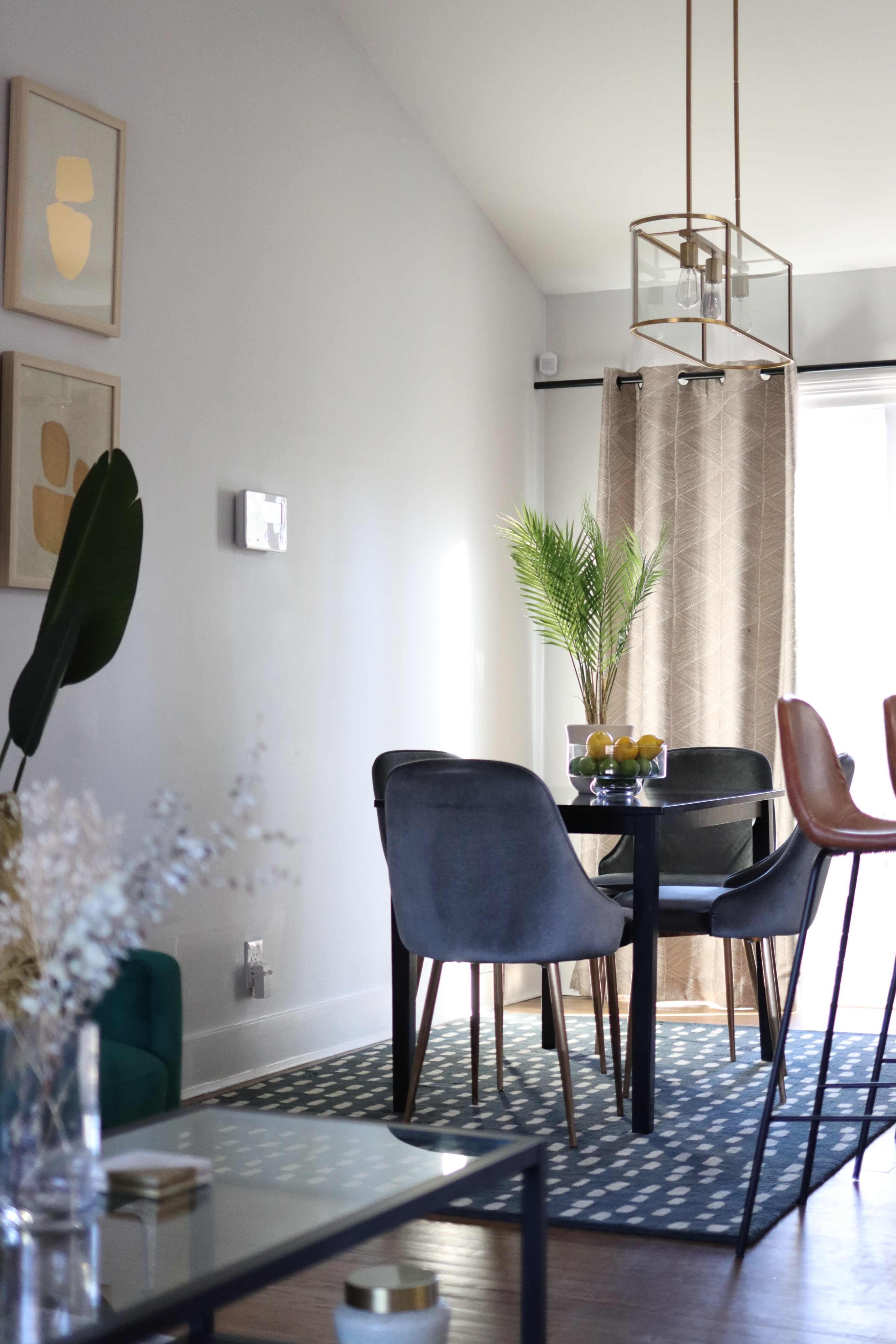 The image depicts a modern dining area featuring a black dining table surrounded by gray chairs, a green plant centerpiece, and framed artwork on the walls.