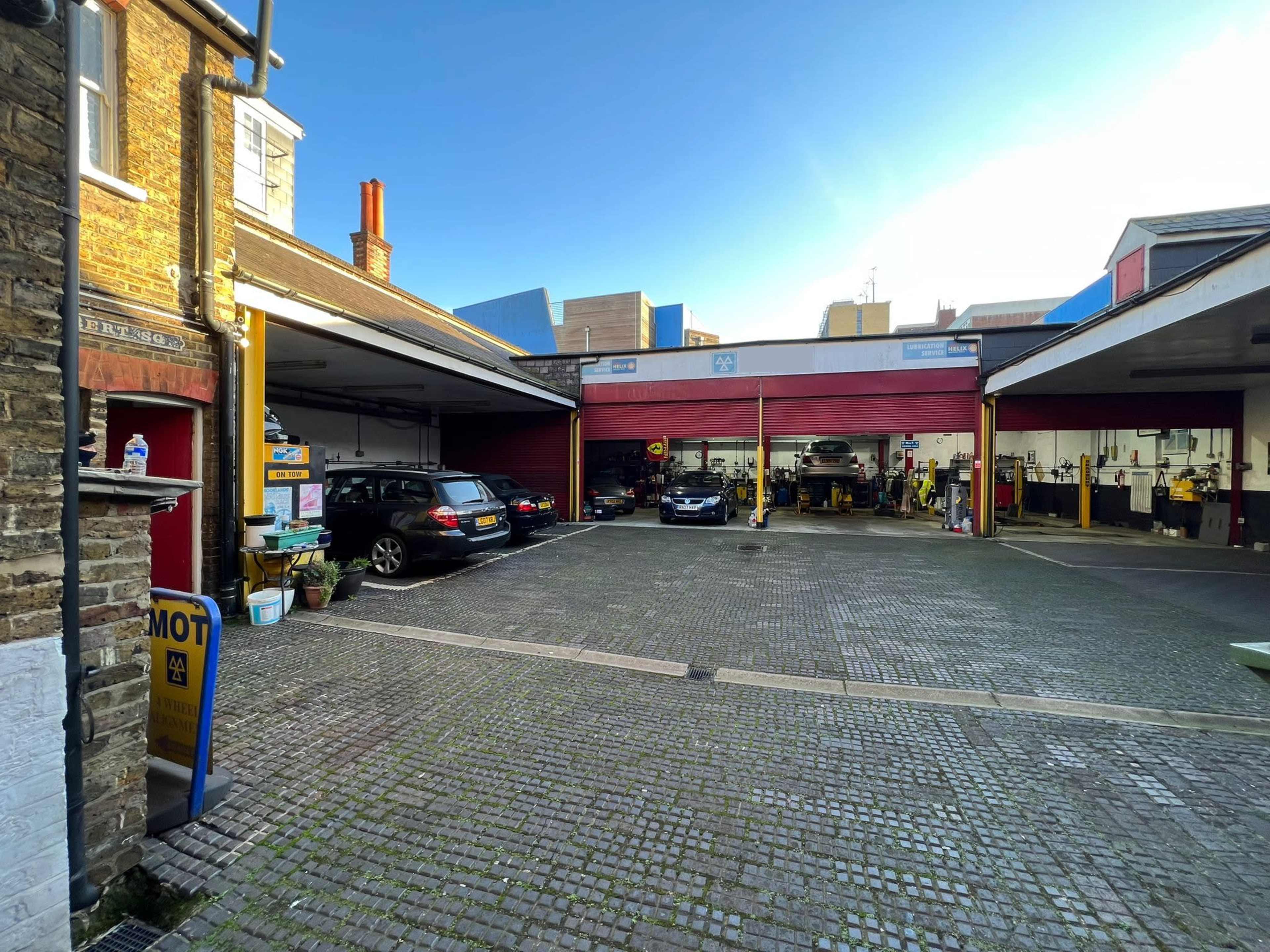 A service garage with several cars, tools, and equipment arranged in a cobblestone courtyard.