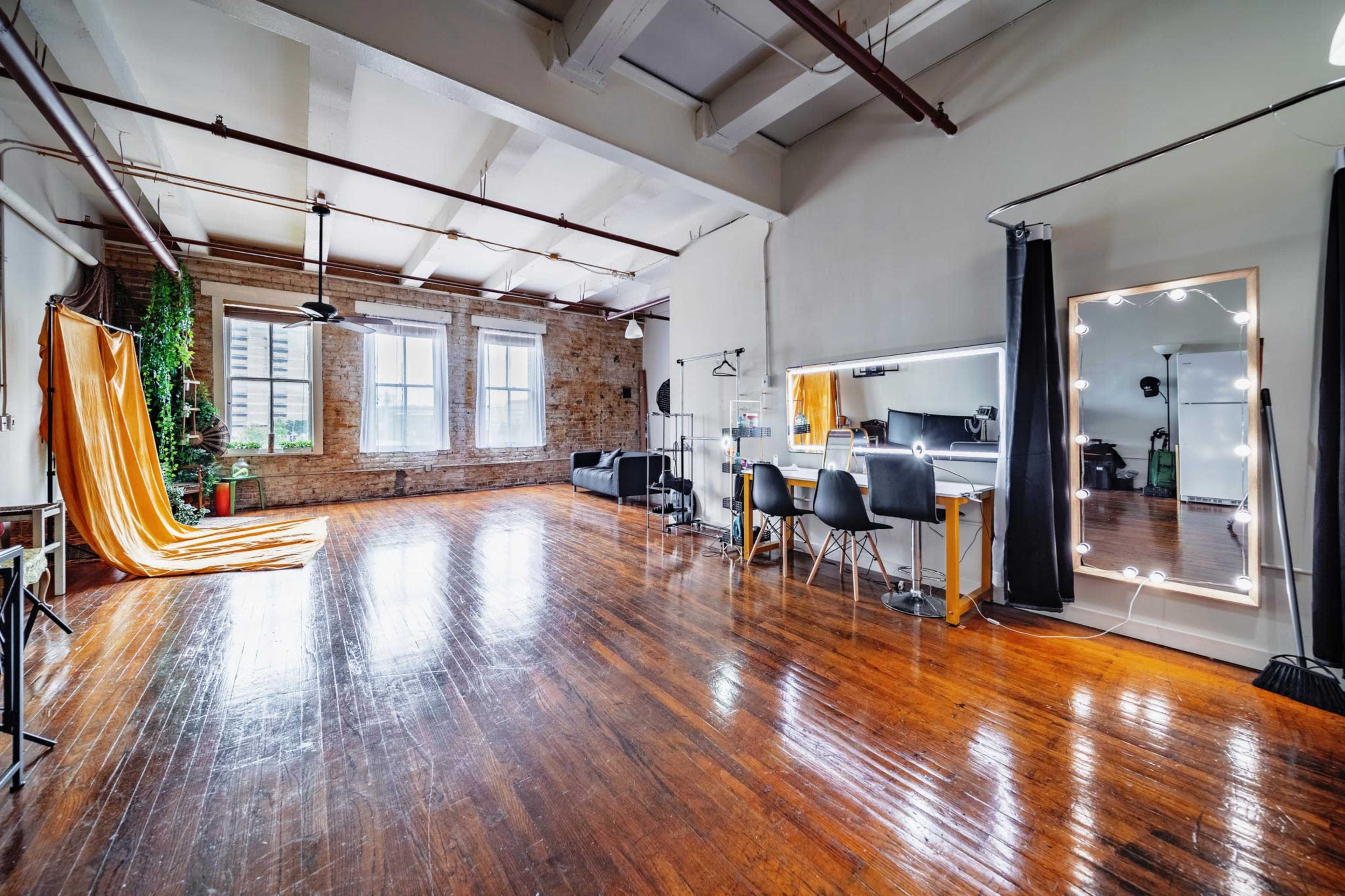 A spacious studio features hardwood floors, large windows, and a small area with a mirror and chairs for activities.