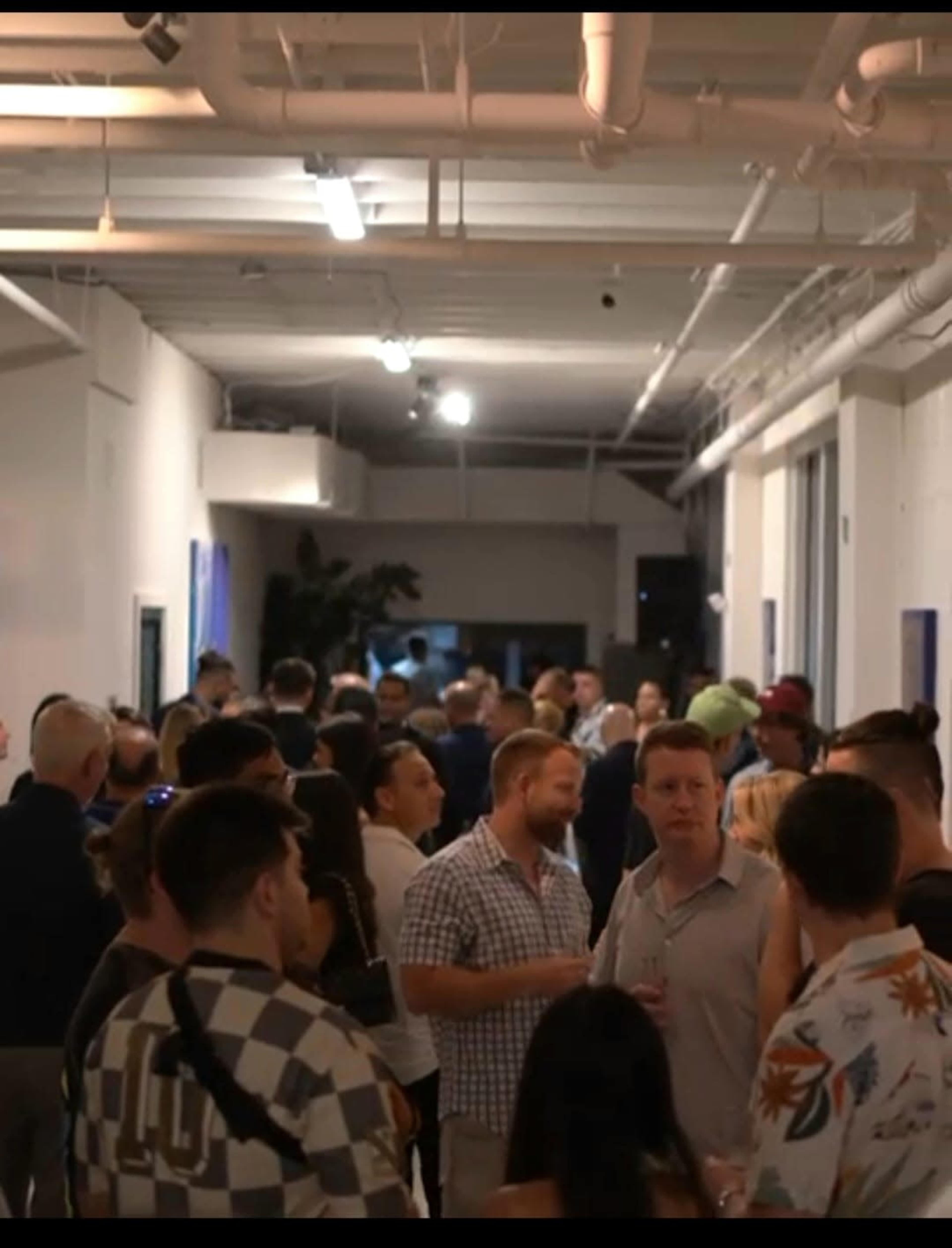 A crowd gathers in a well-lit hallway during a social event, engaging in conversation and networking.