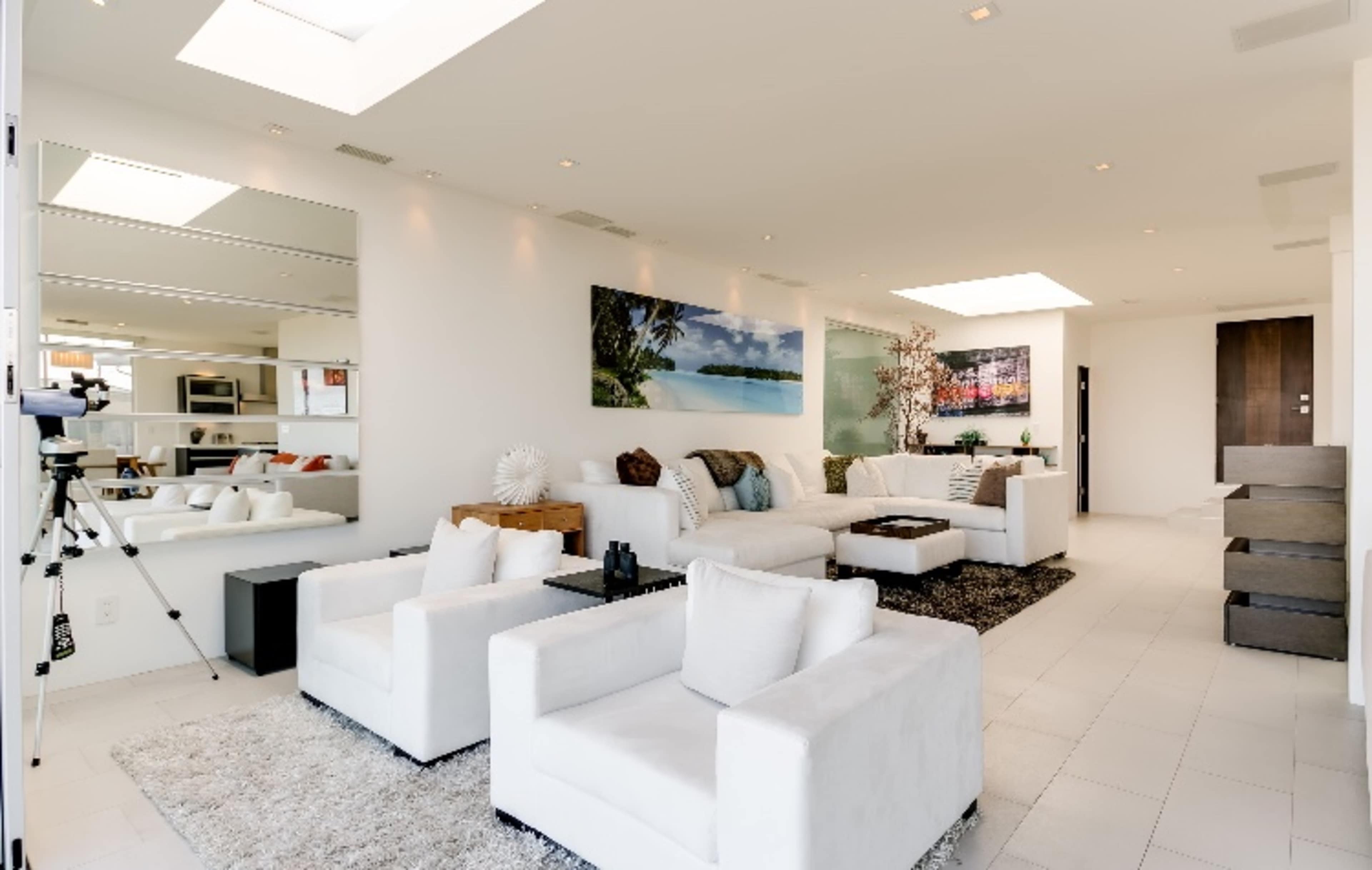 A modern living room with white furniture, large windows, and artwork on the walls.