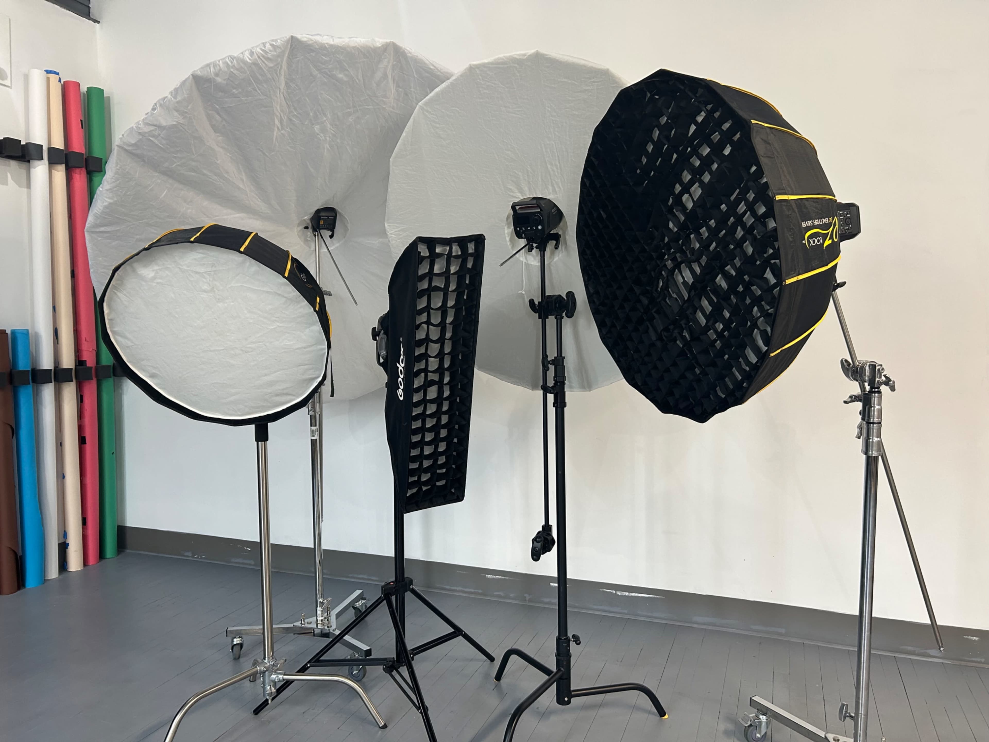 The image shows a photography studio setup featuring three softbox light modifiers on stands, each with different shapes and sizes, along with a black grid for controlling light.