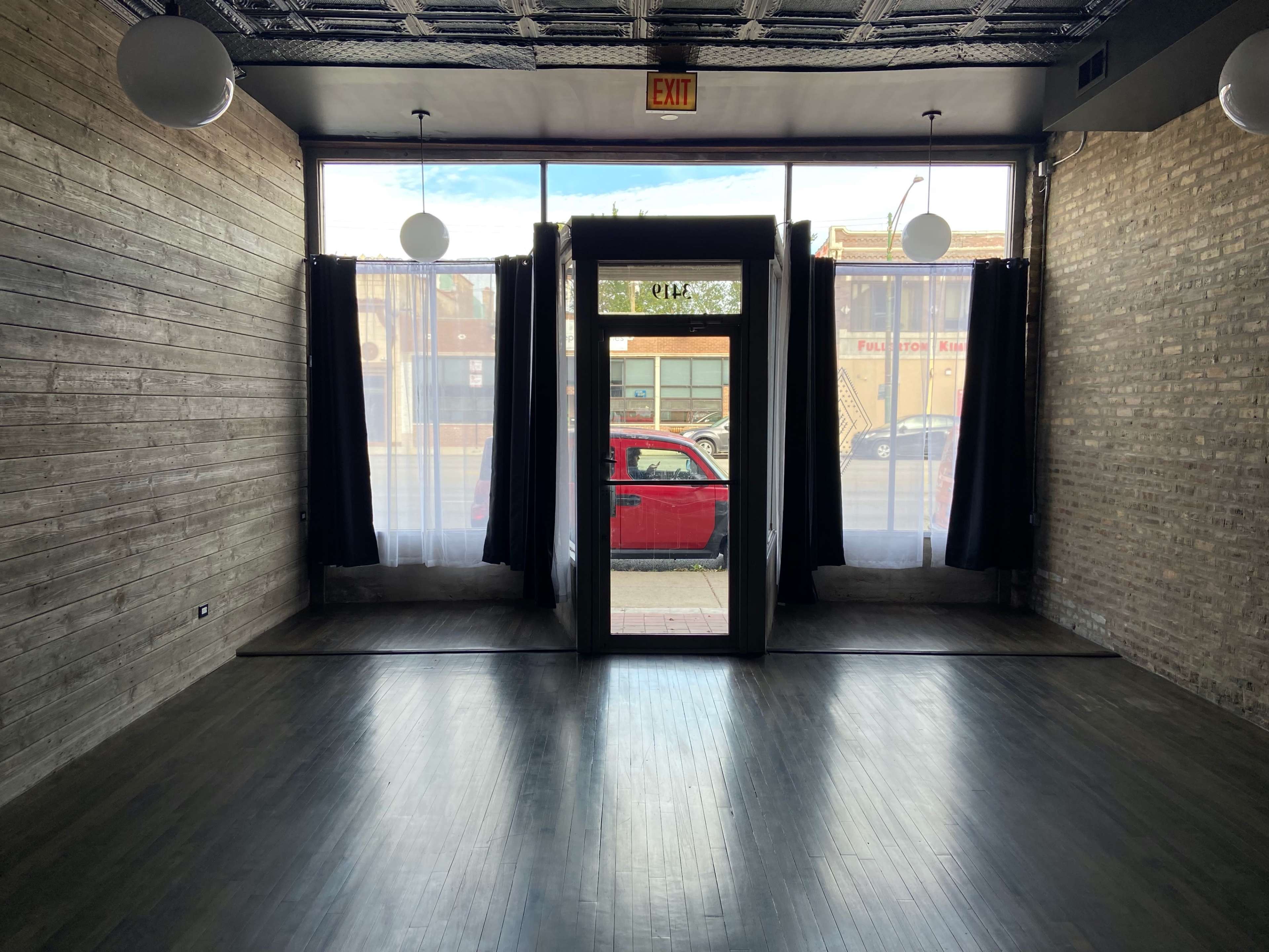 The image shows an empty room with wooden walls and large windows, featuring a door at the center, partially open, and red curtains extending to the sides.