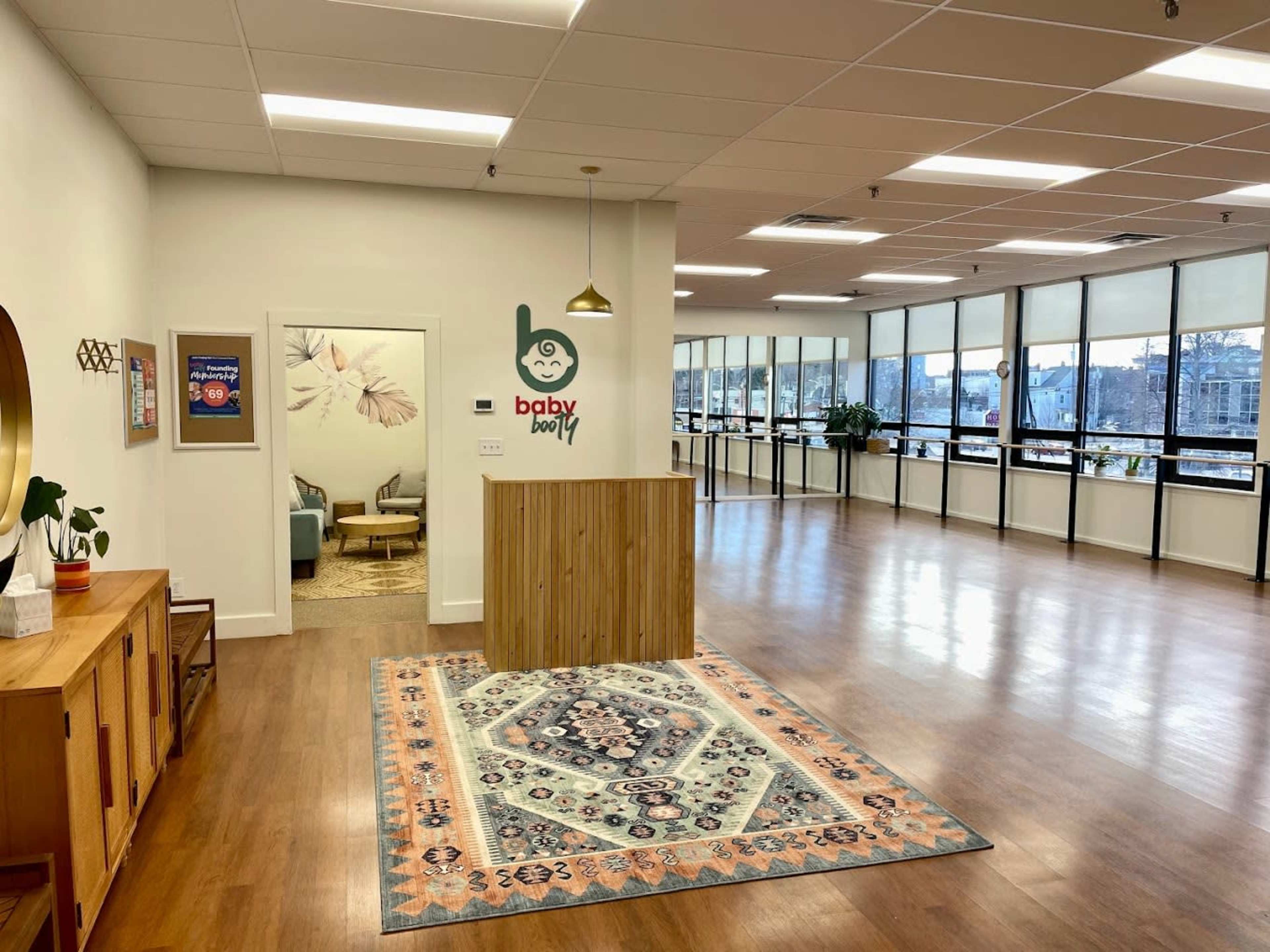 The image shows a spacious, well-lit reception area with a wooden front desk, a large window view, and a decorative rug on the floor.