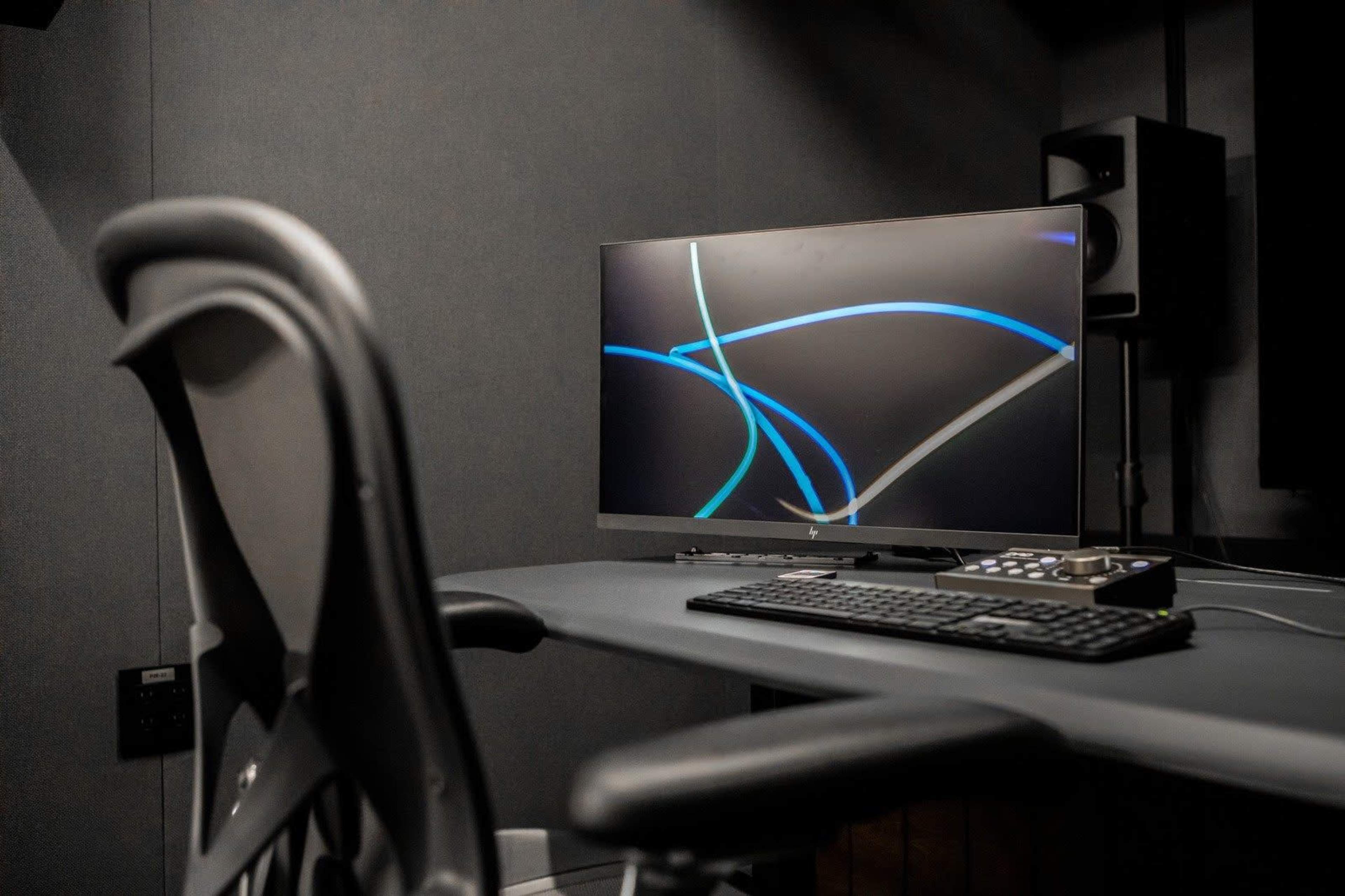 A computer desk features a monitor displaying abstract blue and gray lines, with a keyboard and an ergonomic chair nearby.