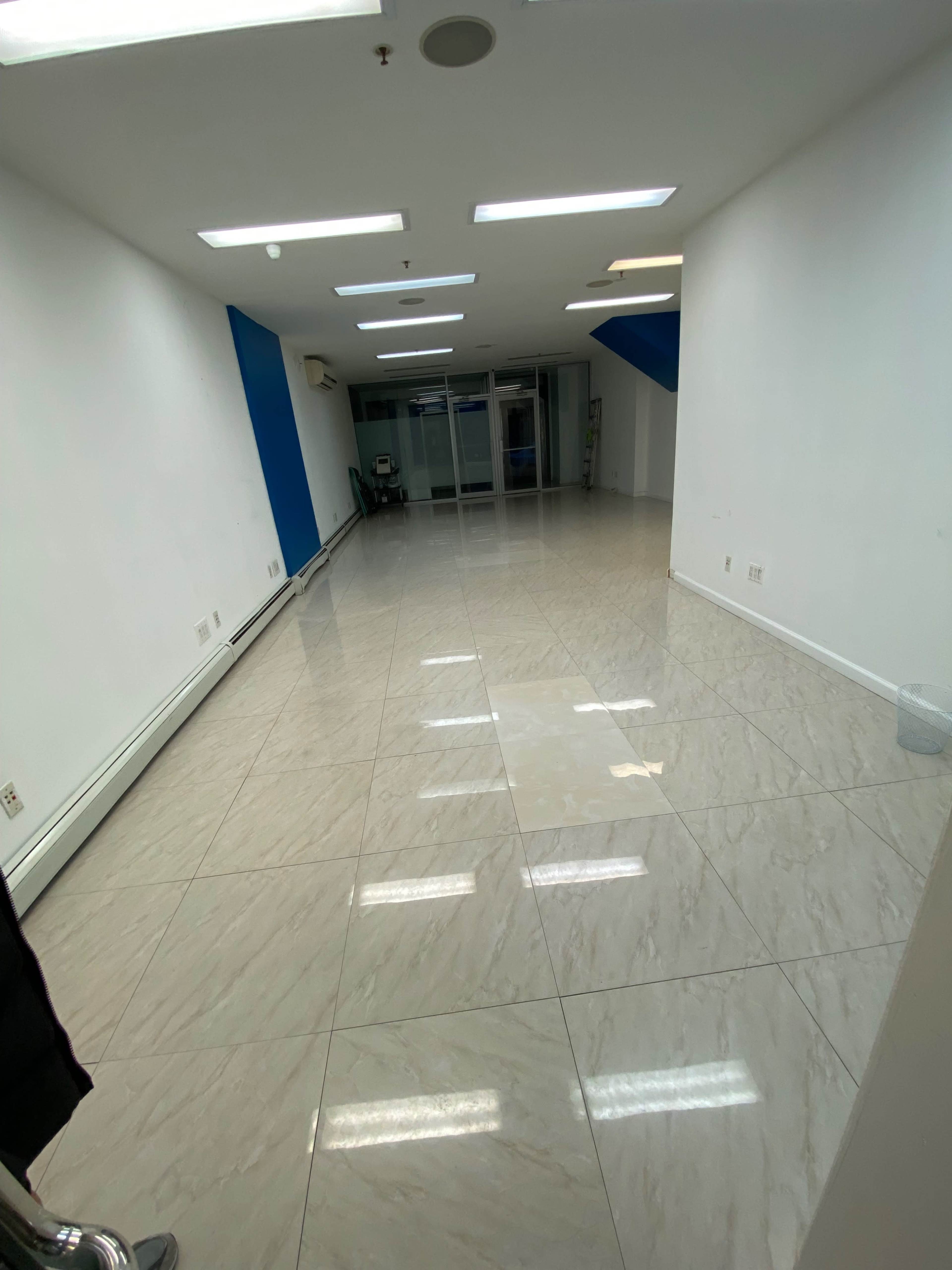 A vacant office space with white walls, glossy tile flooring, and a large window at the far end.