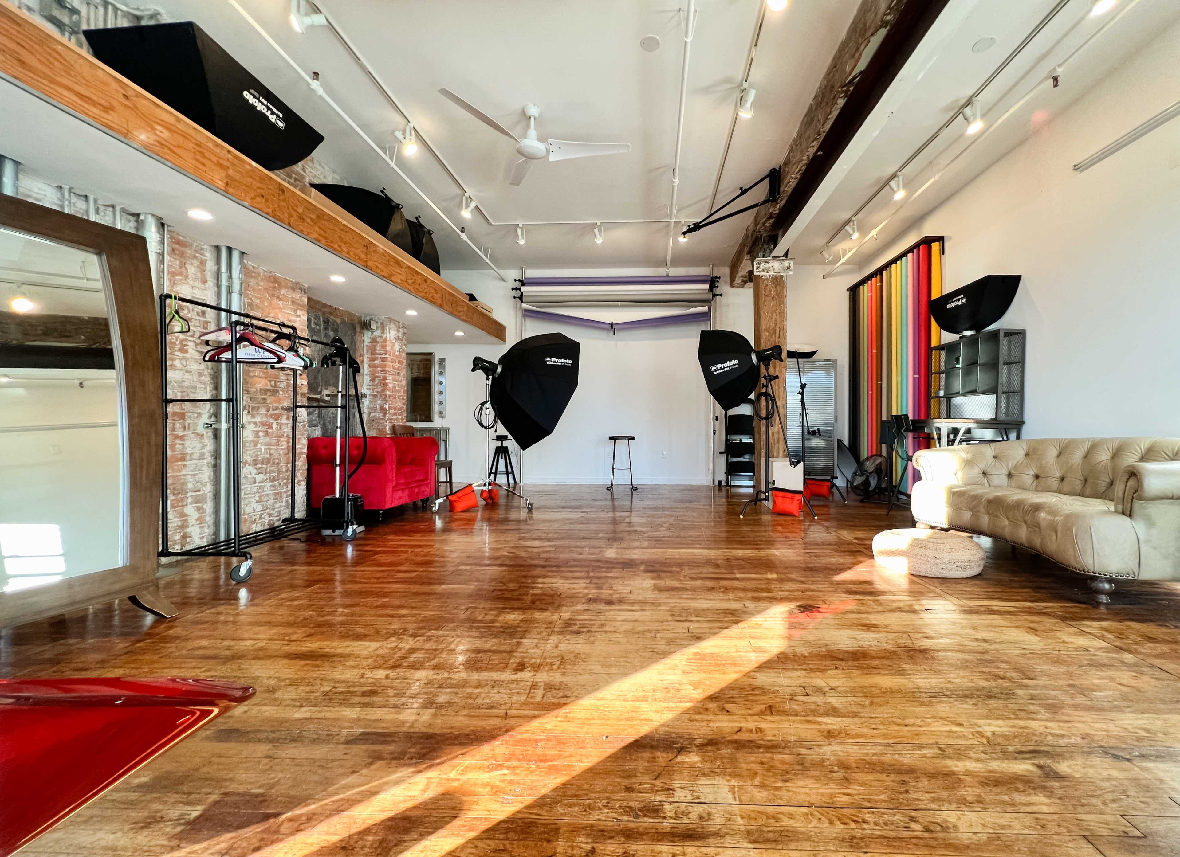 A photography studio featuring a hardwood floor, backdrops, lighting equipment, and furniture arranged in an open space.
