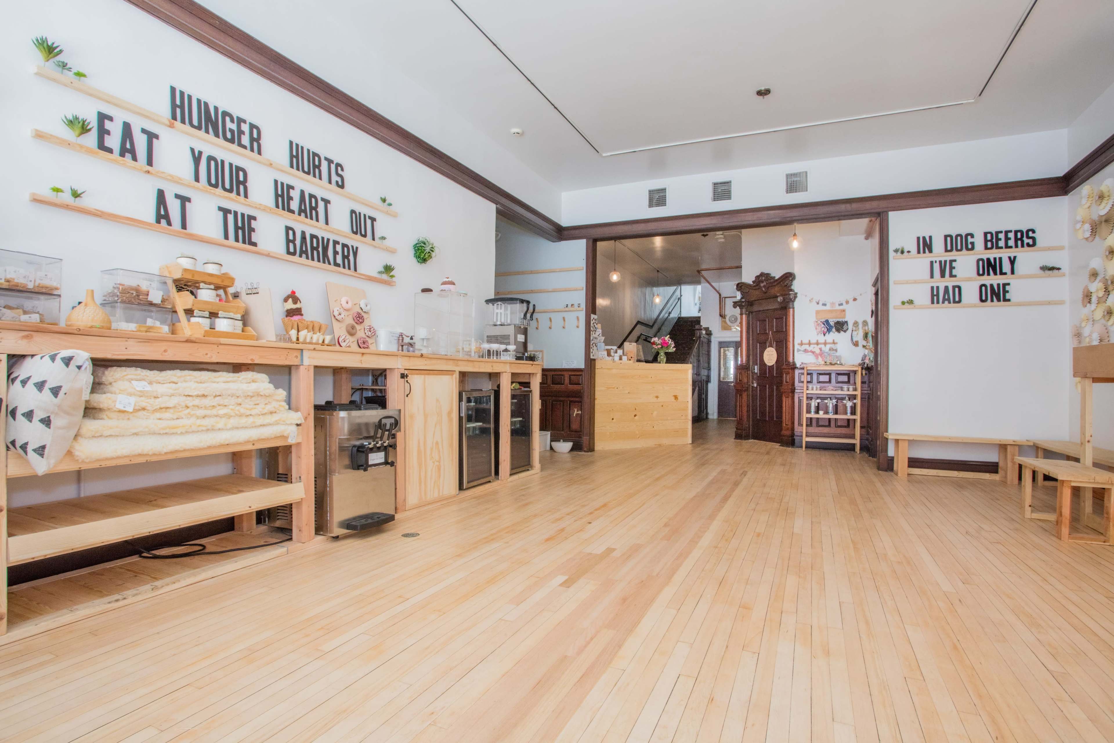 The interior of a pet bakery features wooden counters, a spacious floor, and signage with playful phrases on the walls.