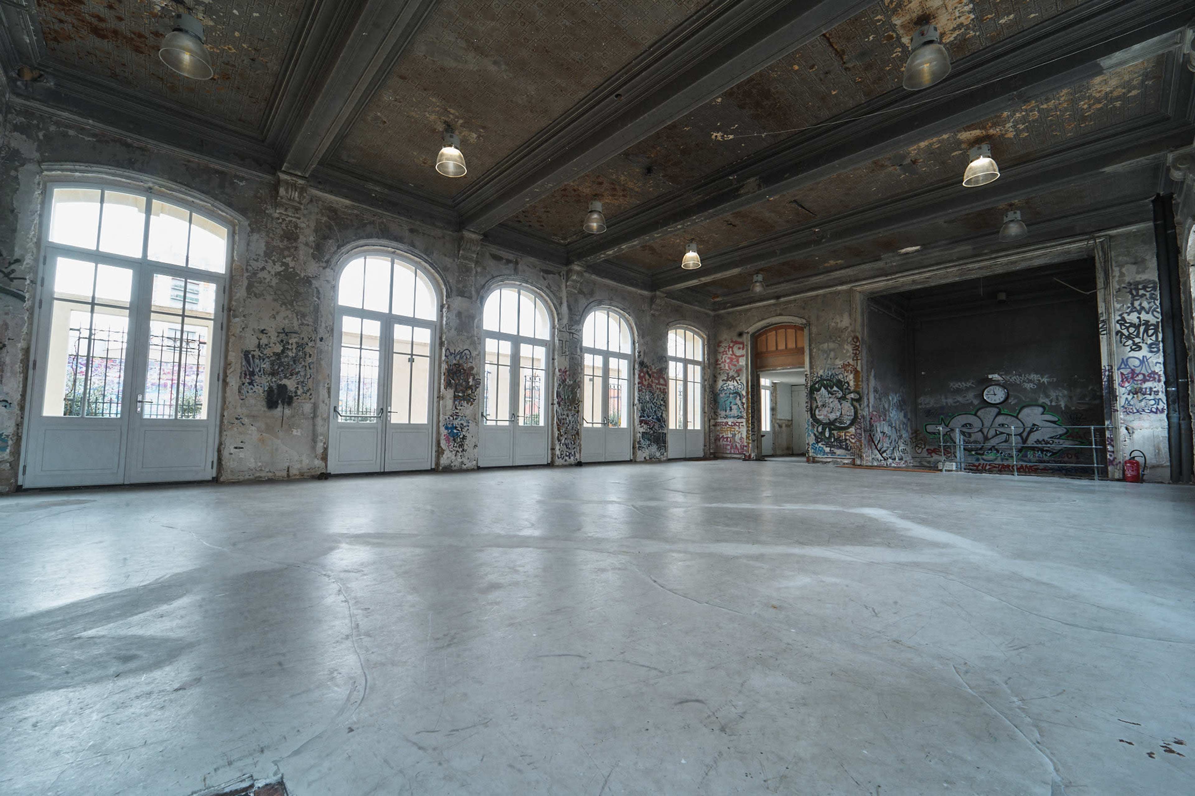 The image shows an empty, dilapidated room with large windows, peeling paint, and graffiti on the walls.