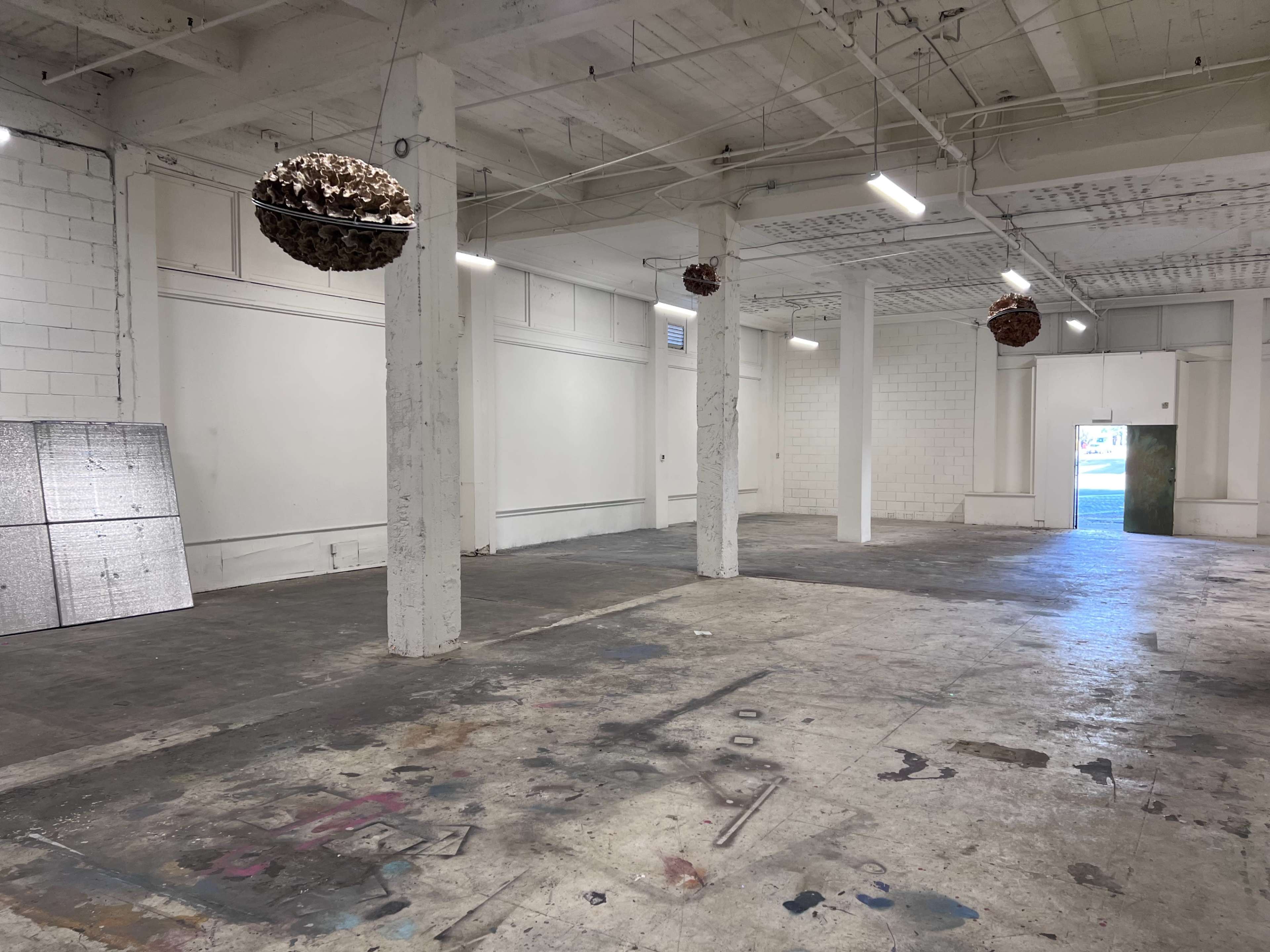 An empty industrial space with concrete floors, exposed beams, and hanging light fixtures.