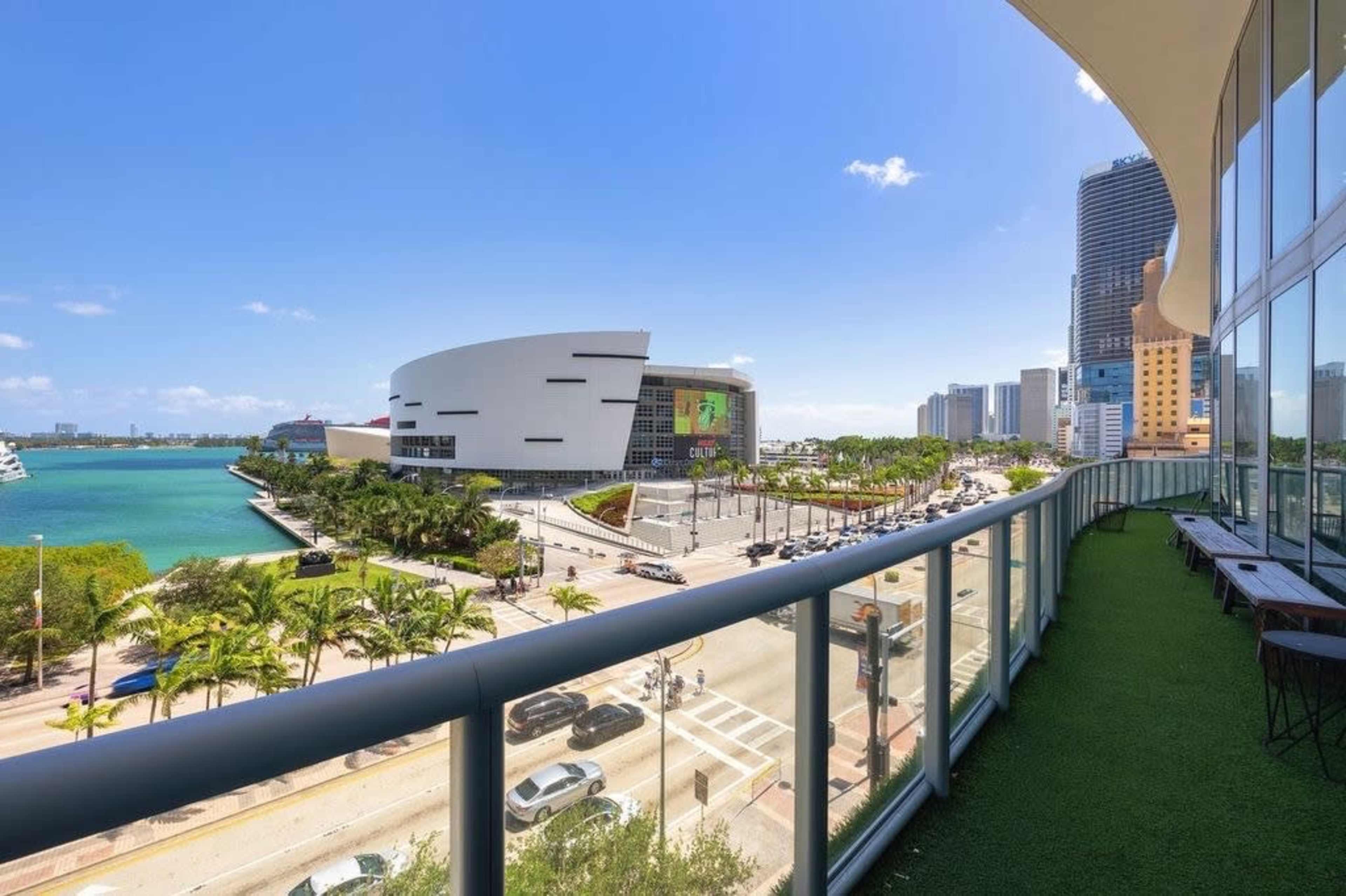 A balcony view overlooking a coastal area, with a modern building in the foreground and city skyline in the background.