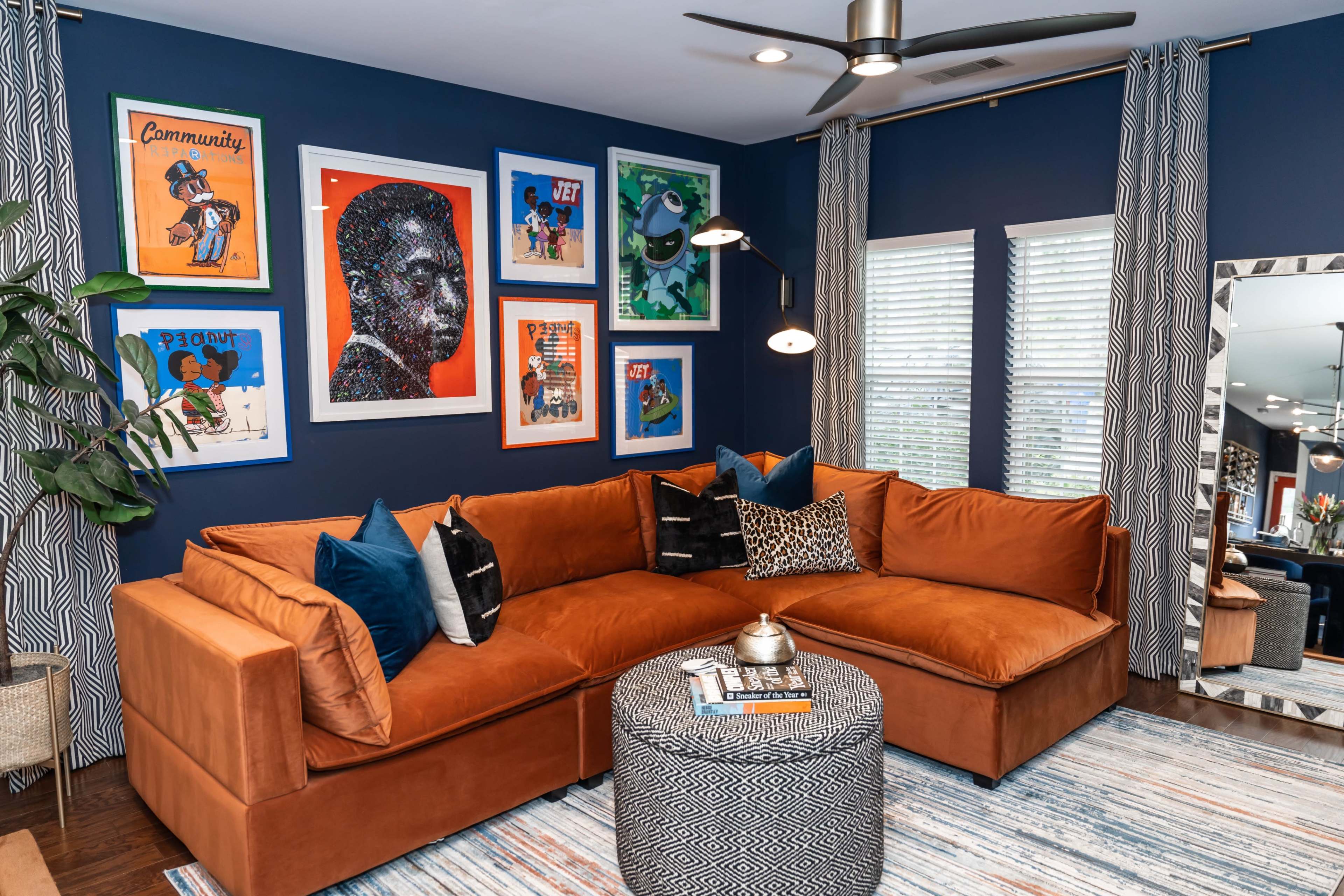 The image shows a cozy living room featuring a sectional sofa, colorful framed artwork on a blue wall, and a round coffee table with decorative items.