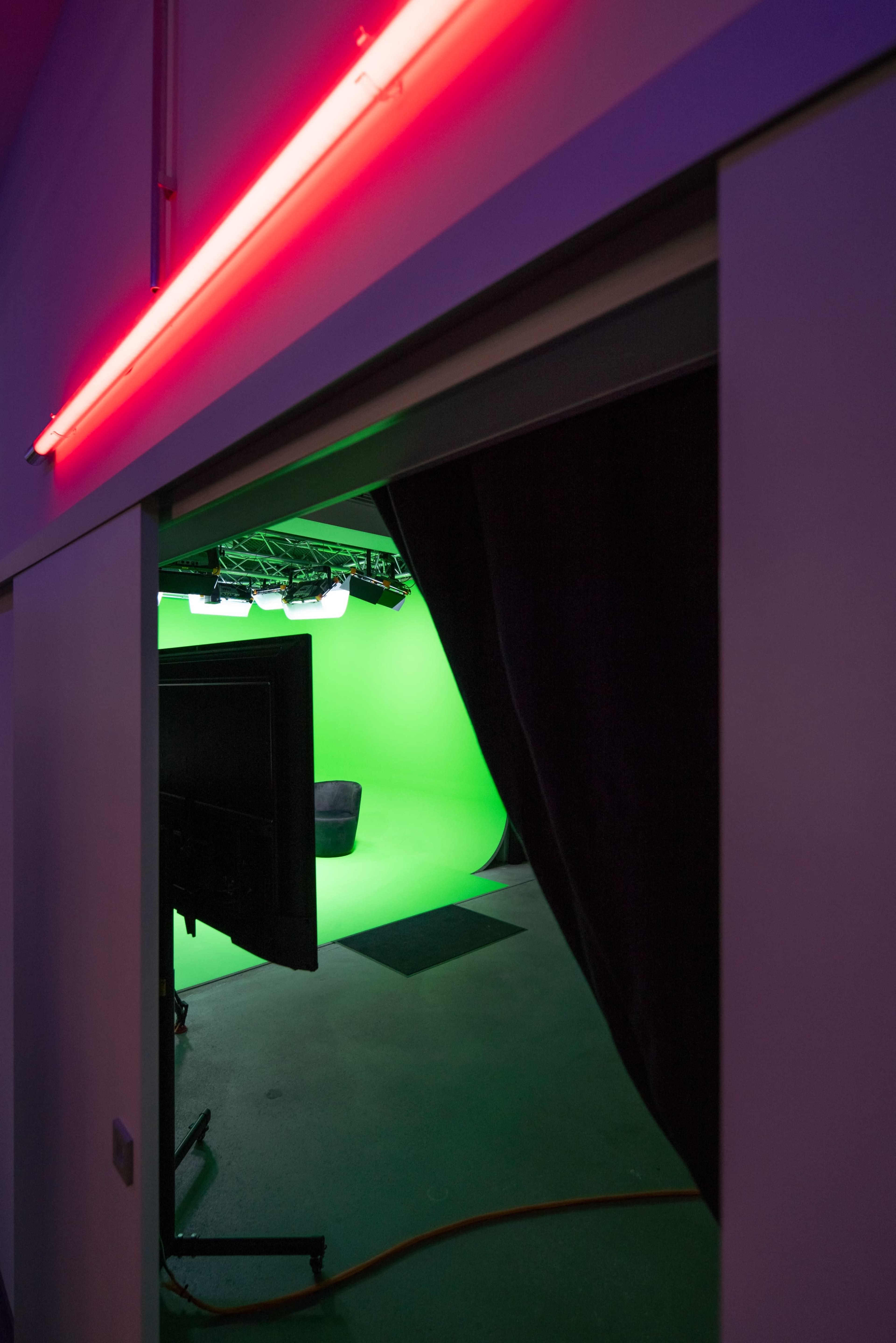 A doorway leads into a green screen studio with a television monitor visible in the foreground.