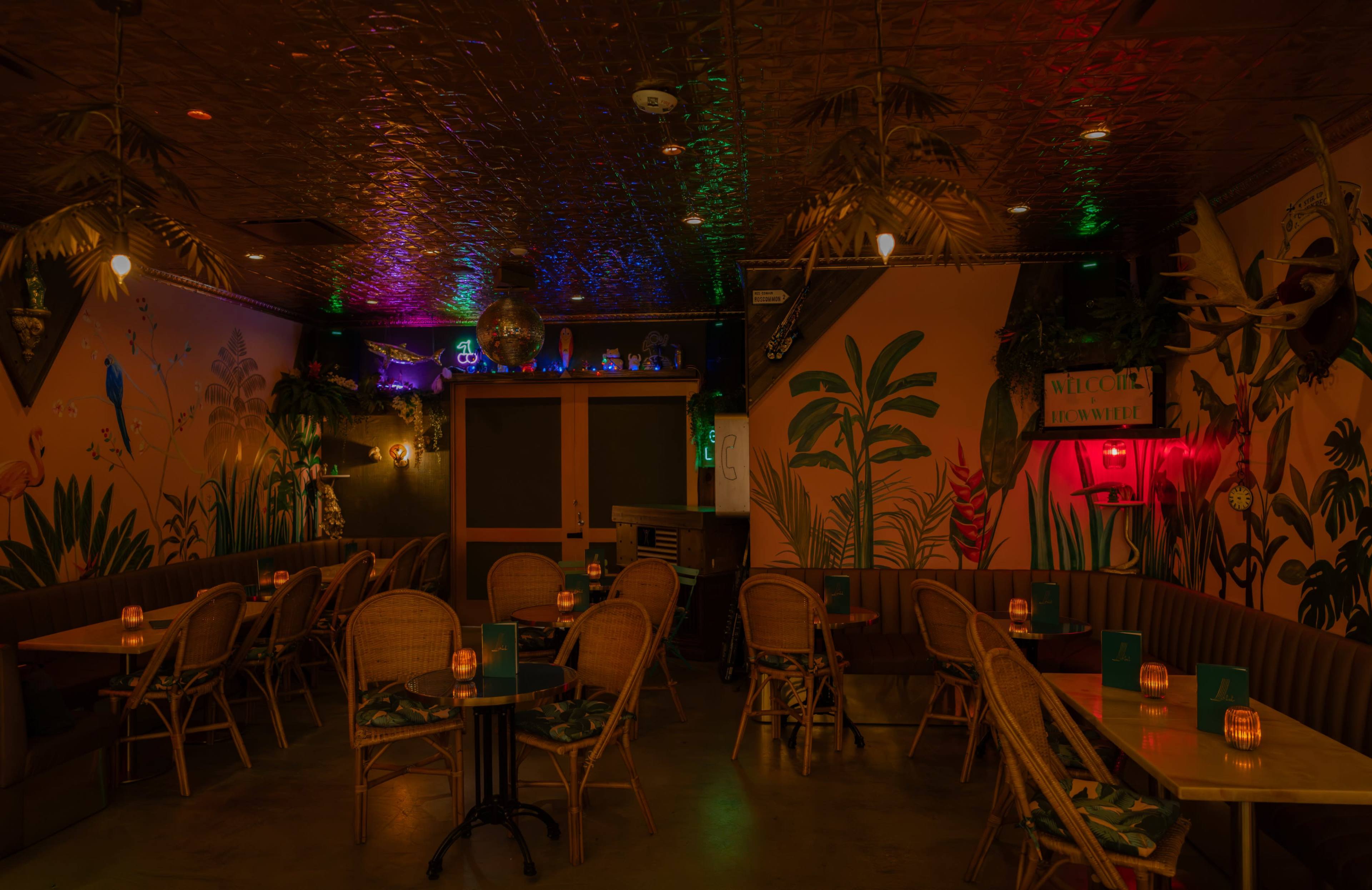 The image shows a dimly lit restaurant interior with tropical-themed decor, featuring rattan chairs and ambient lighting.