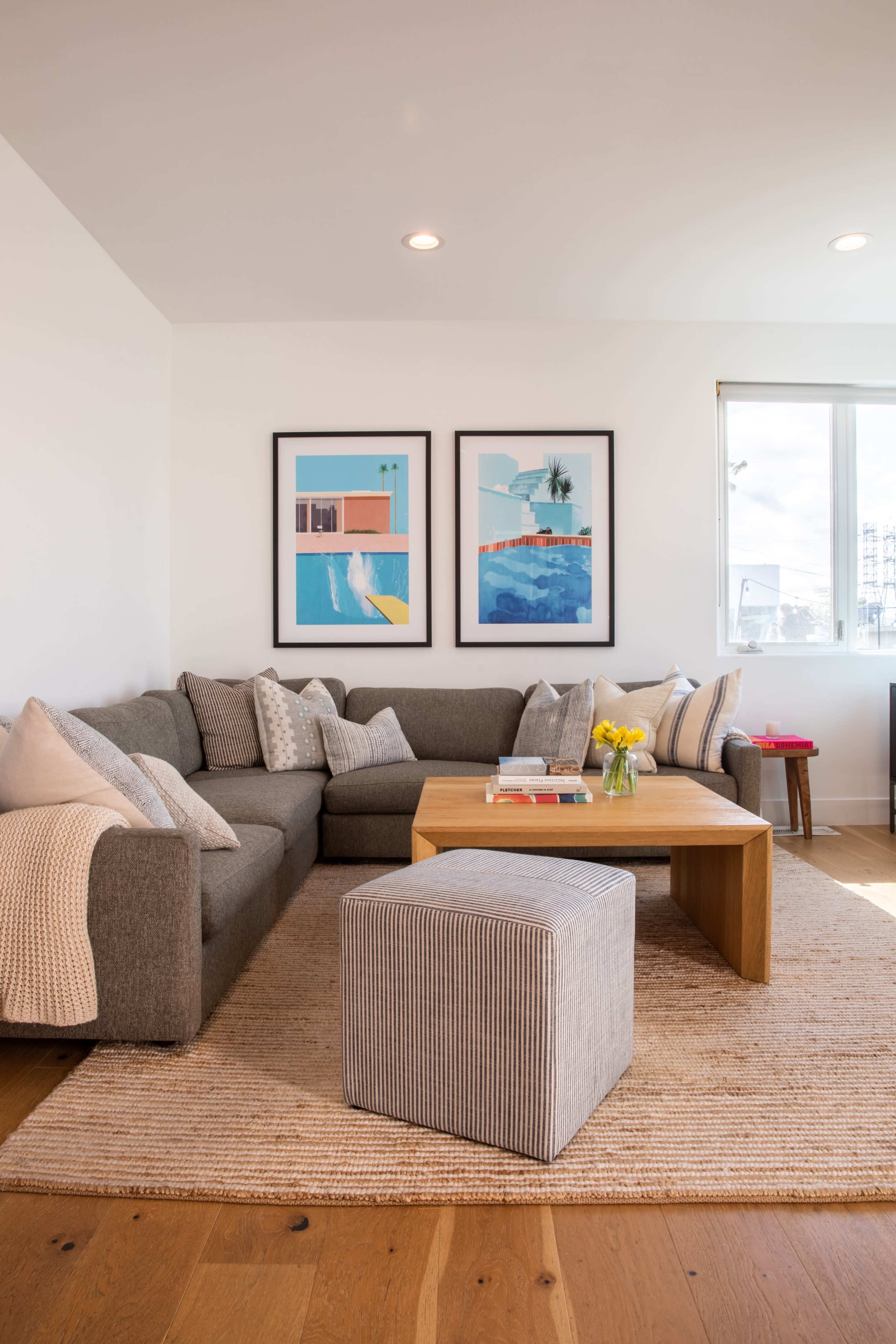 A modern living room with a gray sectional sofa, a wooden coffee table, and two framed artworks on the wall.