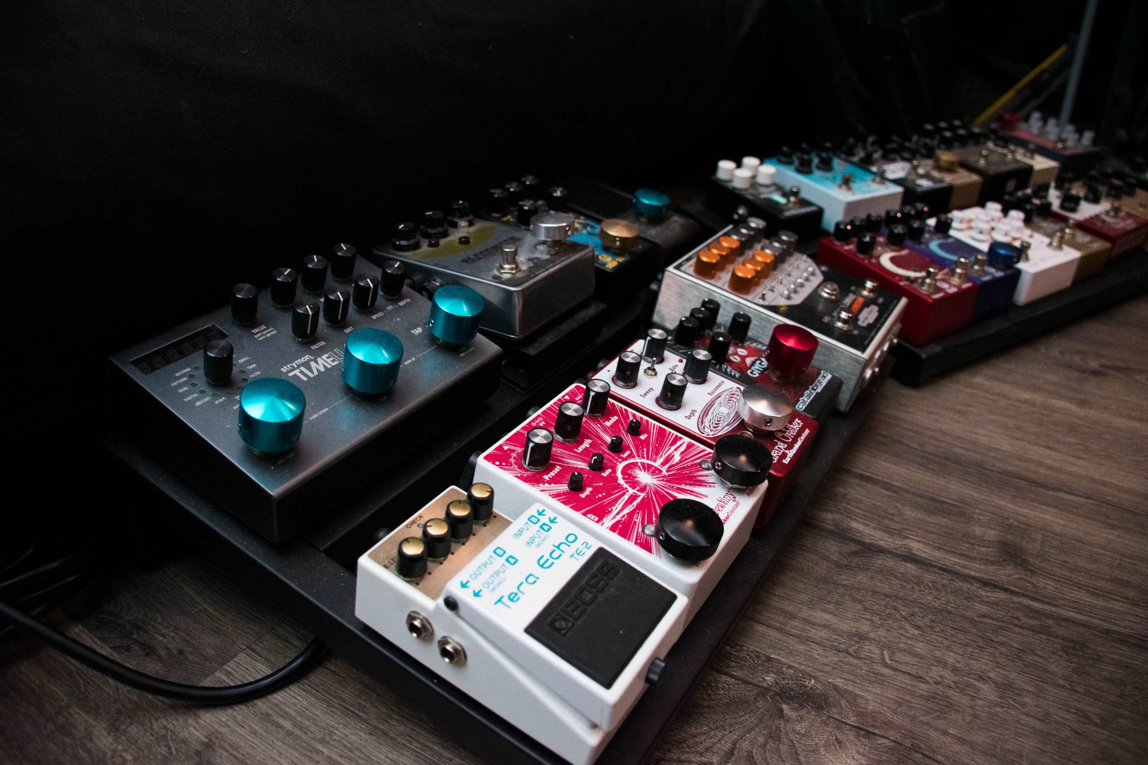 The image displays a collection of guitar effects pedals arranged on a pedalboard with various knobs and buttons.