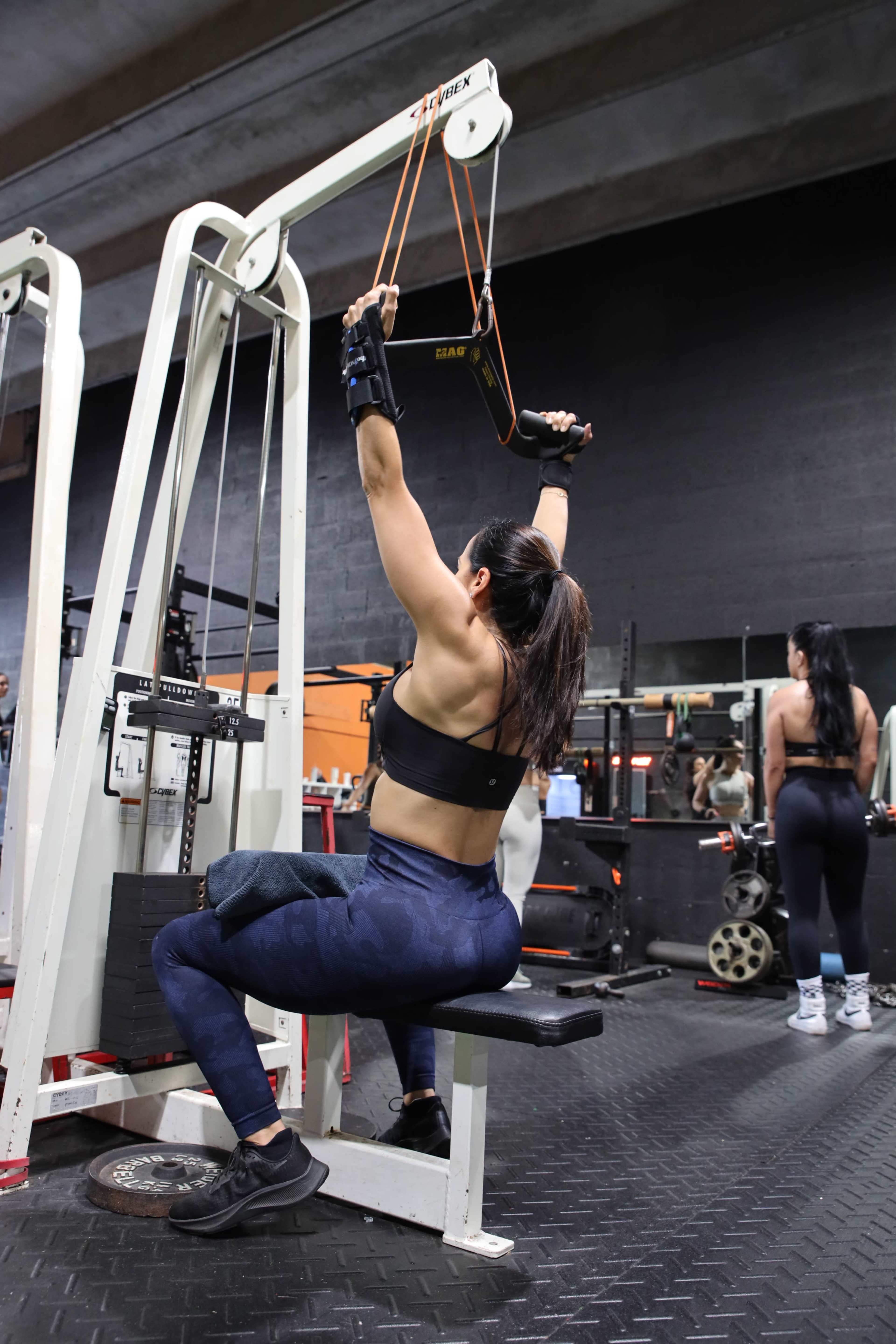 A woman in workout attire is using a cable machine for exercise in a gym setting.
