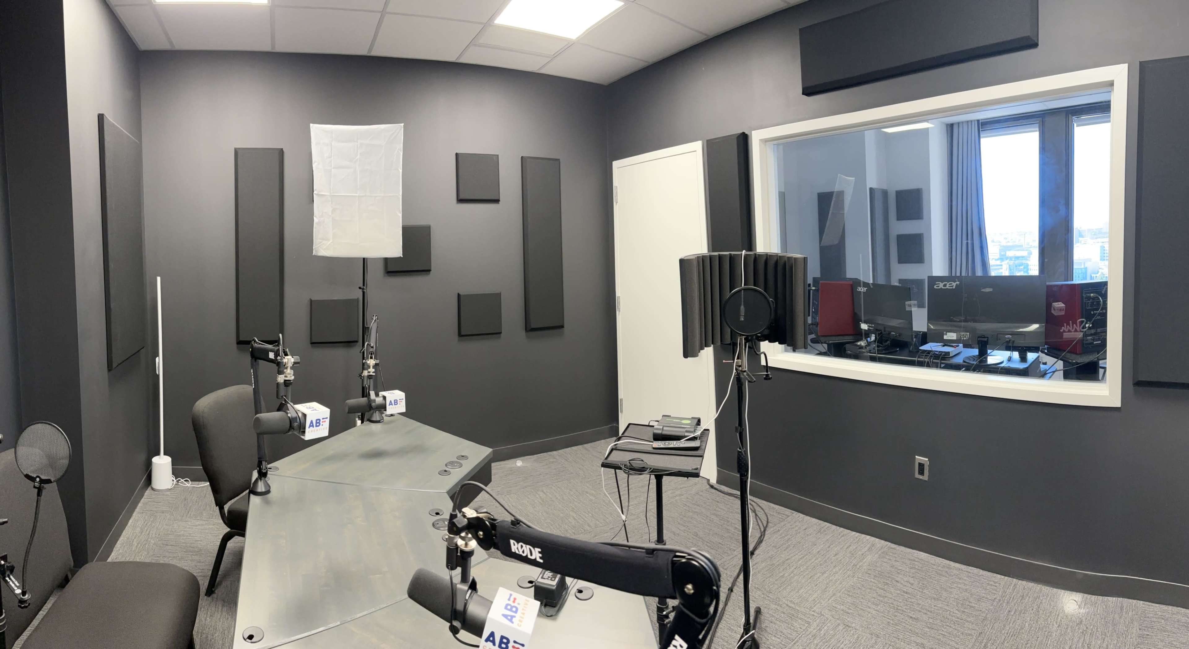A soundproof recording studio equipped with microphones, a glass observation window, and sound-absorbing panels on the walls.