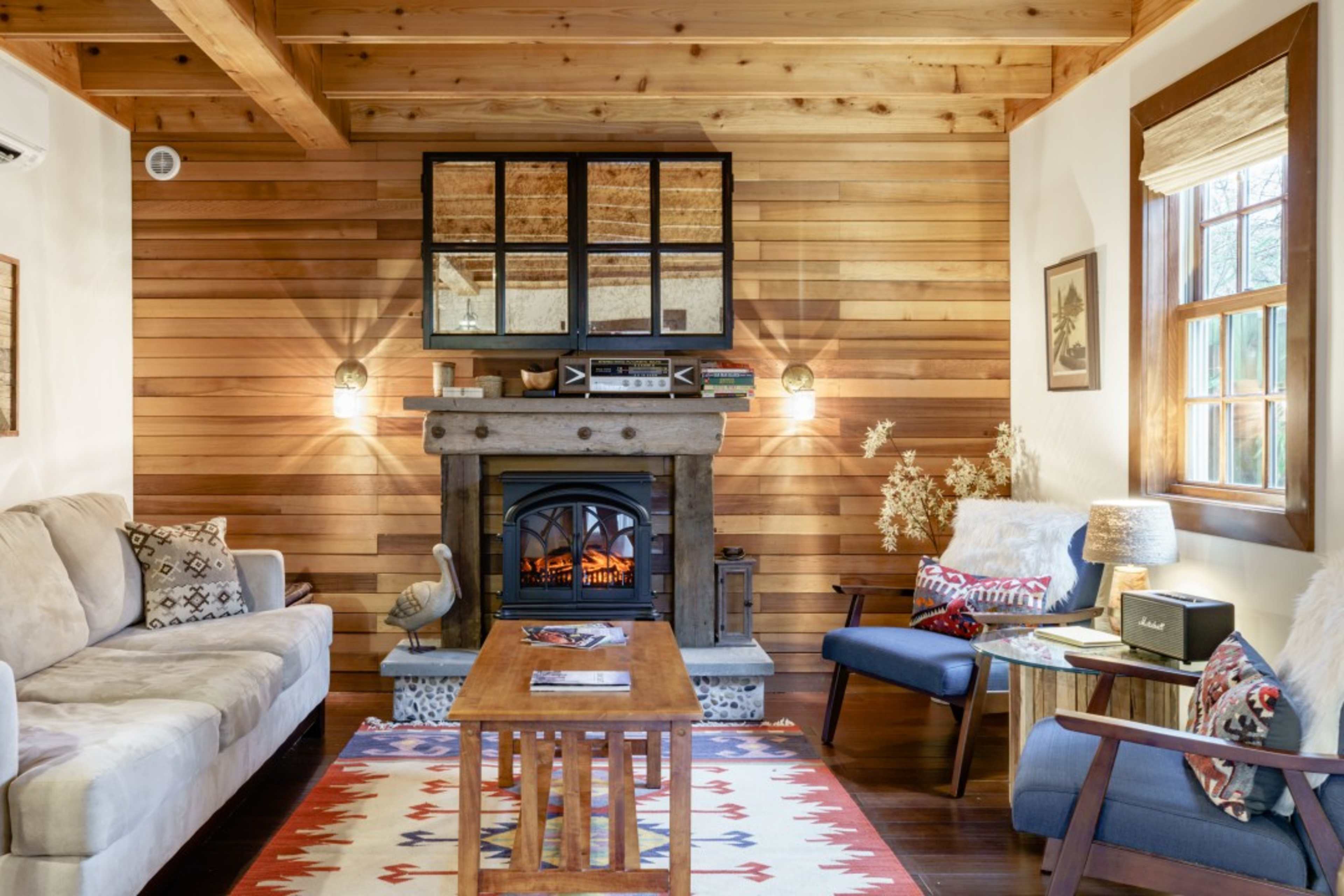 A cozy living room with wooden walls, a fireplace, and a wooden coffee table surrounded by various seating options.