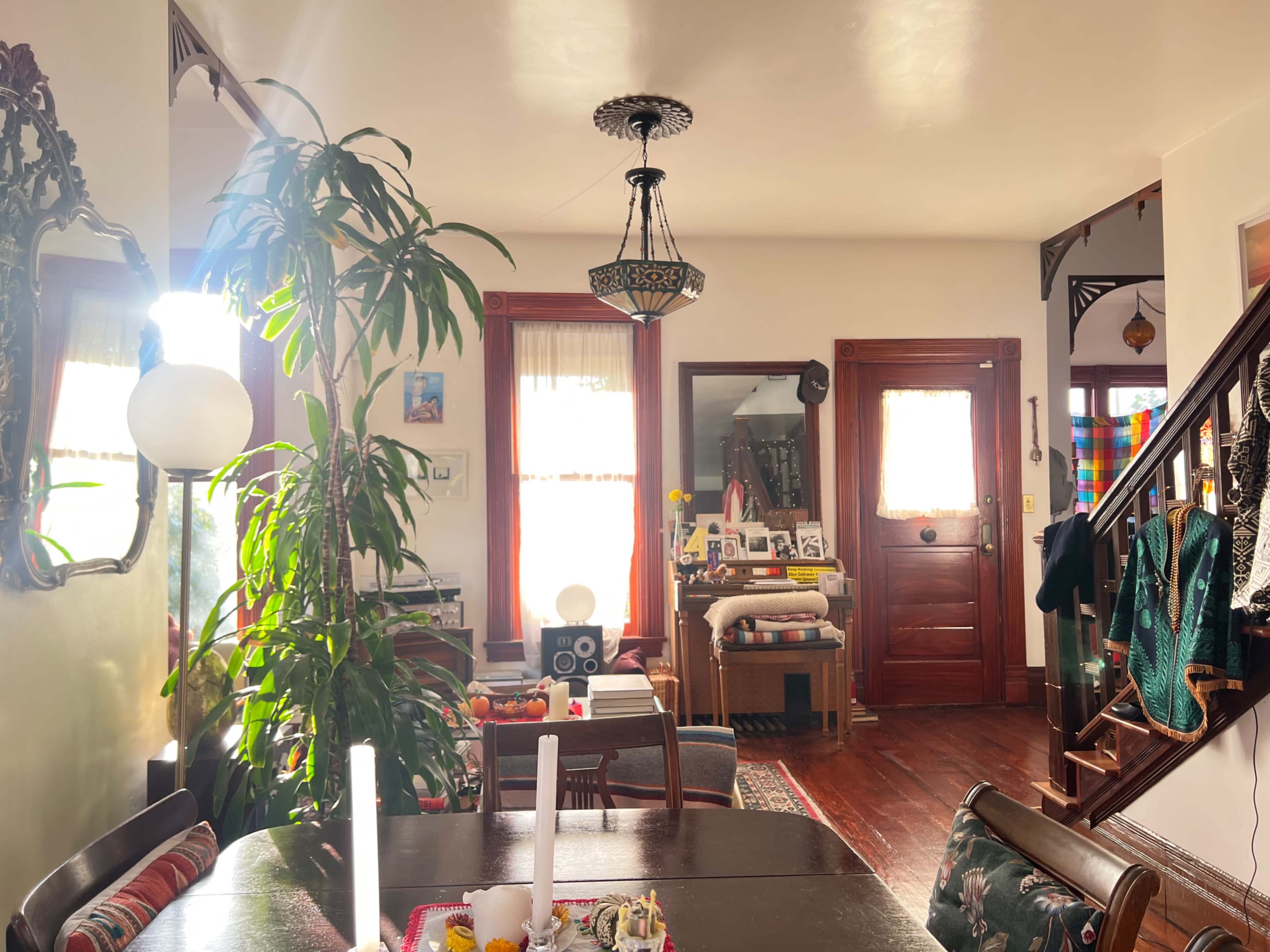 A well-lit living space featuring a dining table with candles, a large indoor plant, and a staircase leading to an upper level adorned with decorative items.