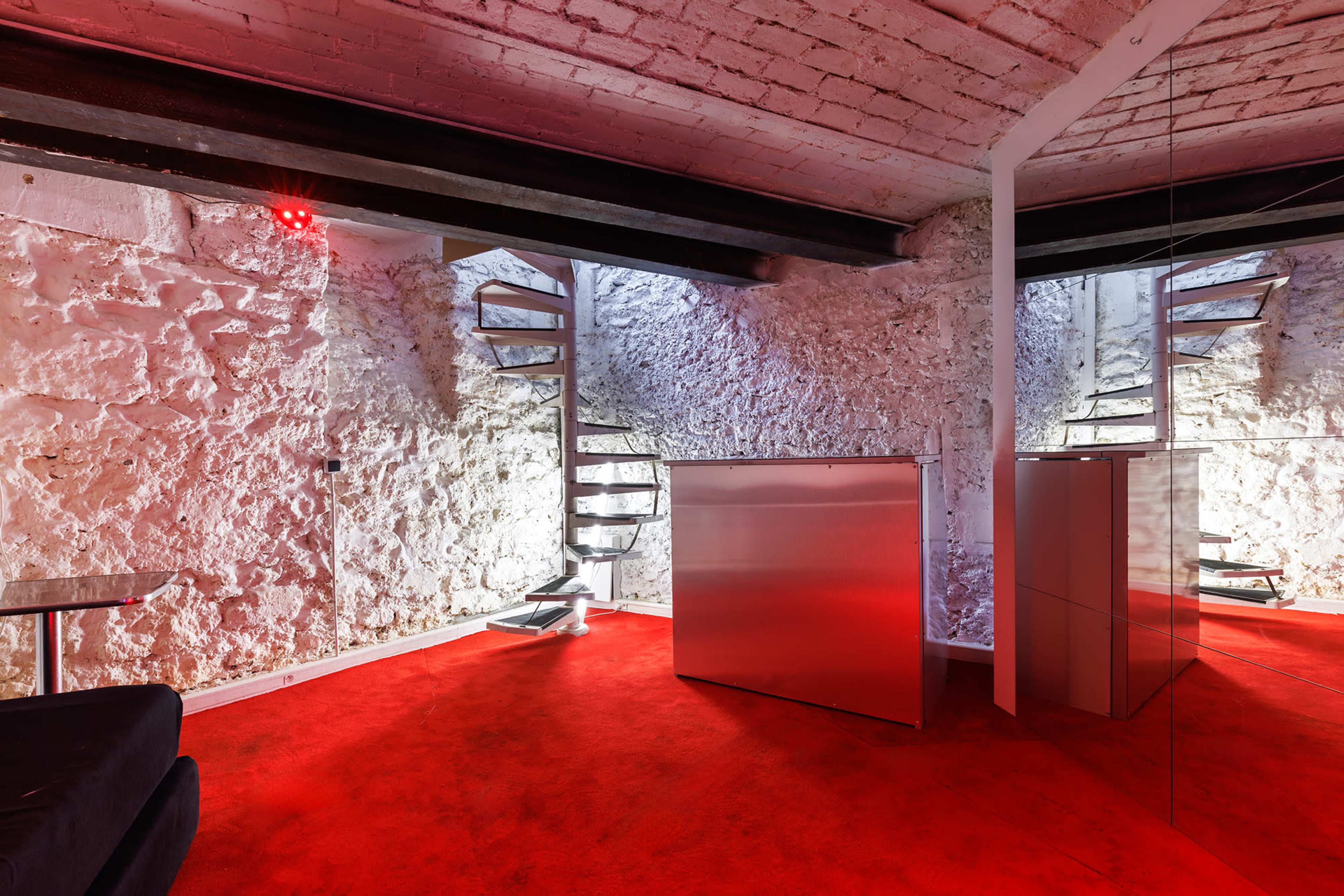 The image shows a modern interior space featuring red carpet, white textured walls, and a spiral staircase leading to an upper level.