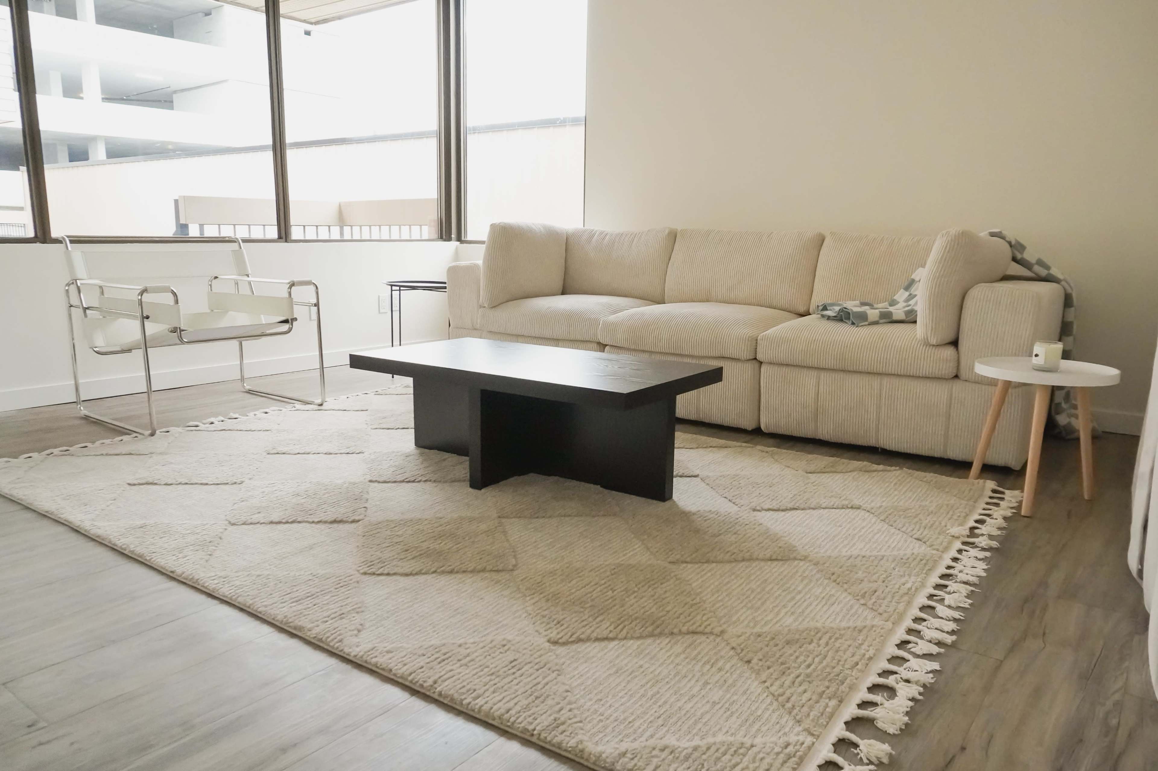 A modern living room with a beige sectional sofa, a black coffee table, an armchair, and a light-colored rug.