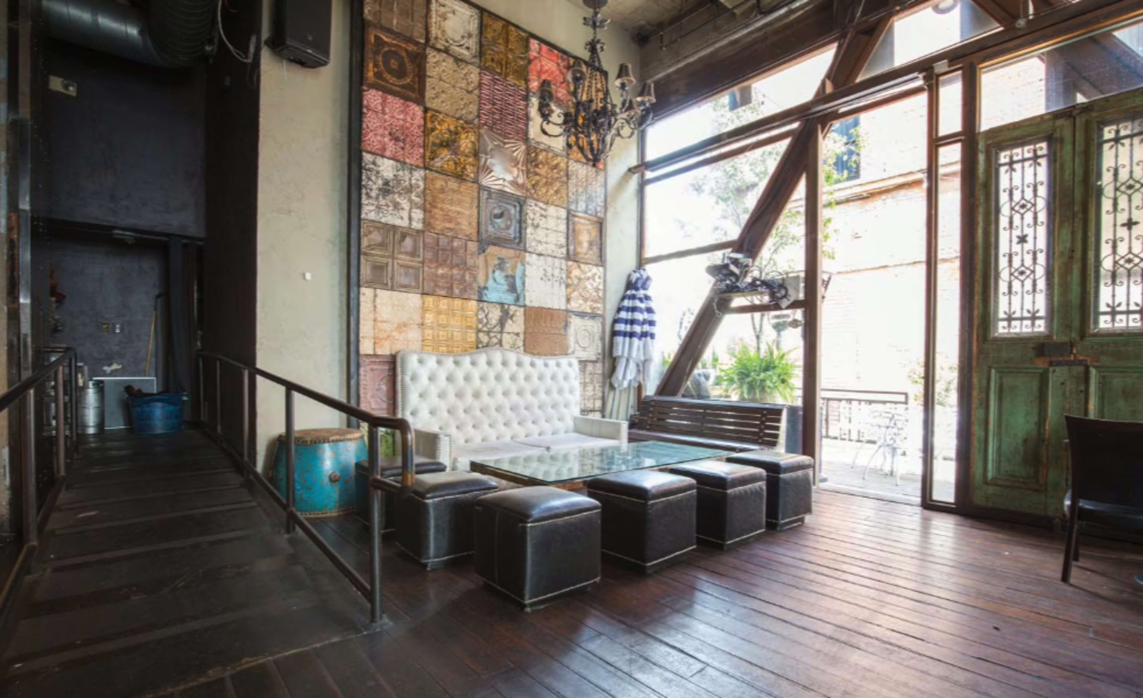 The image shows a modern interior with a white tufted sofa, black ottomans, and a decorative wall featuring patterned tiles.