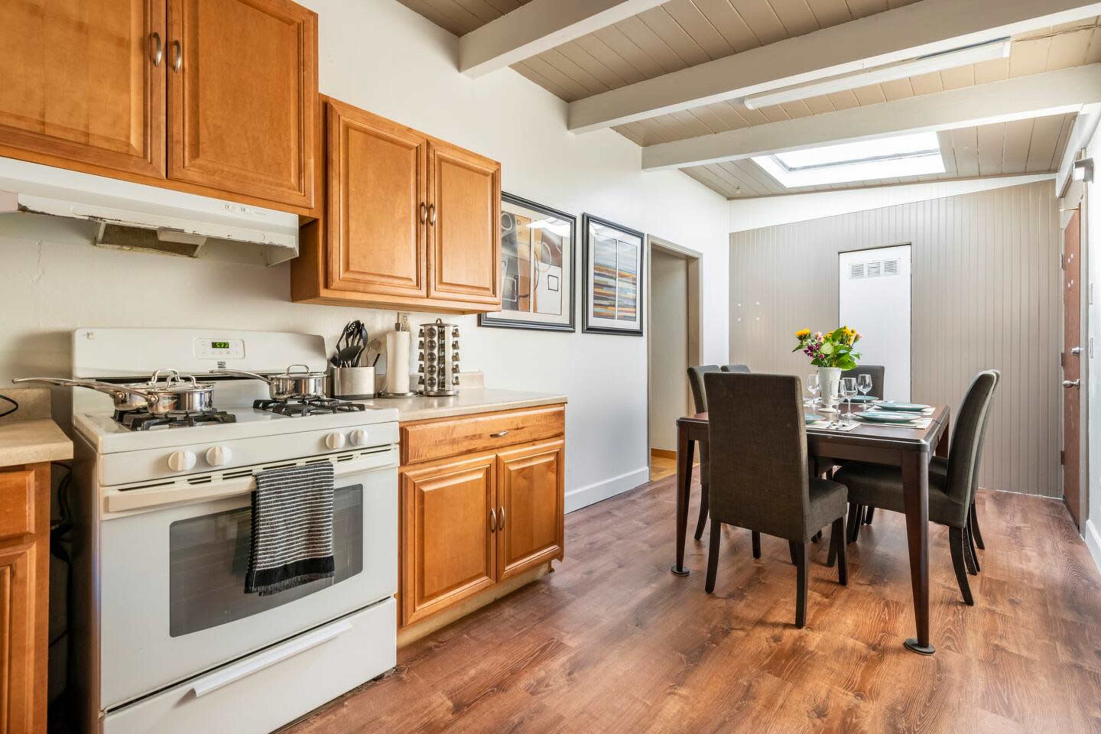 A kitchen and dining area featuring wooden cabinetry, a stove, and a dining table set for a meal.