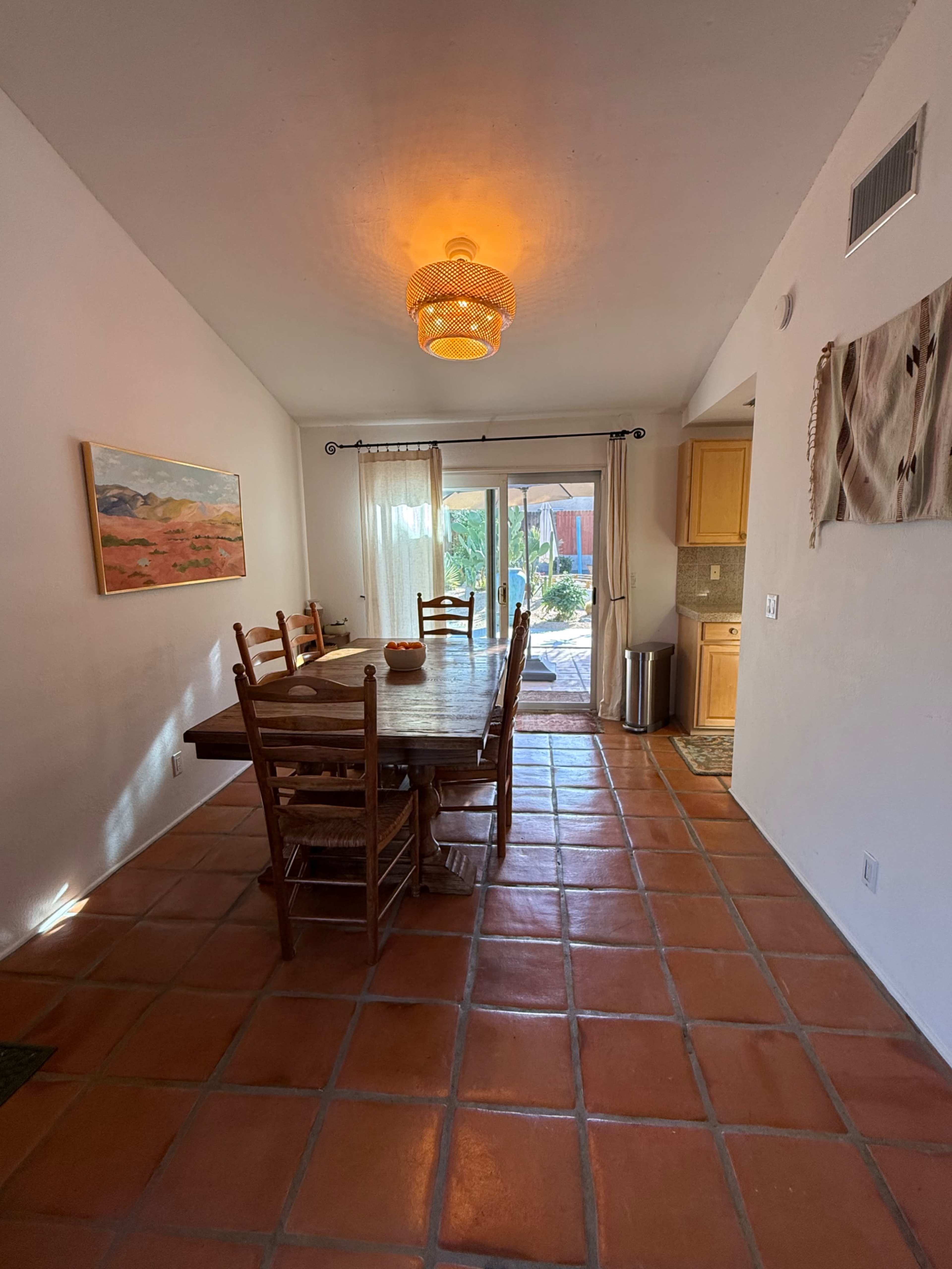 A dining area features a long wooden table surrounded by chairs, with a sliding glass door leading to an outdoor space.