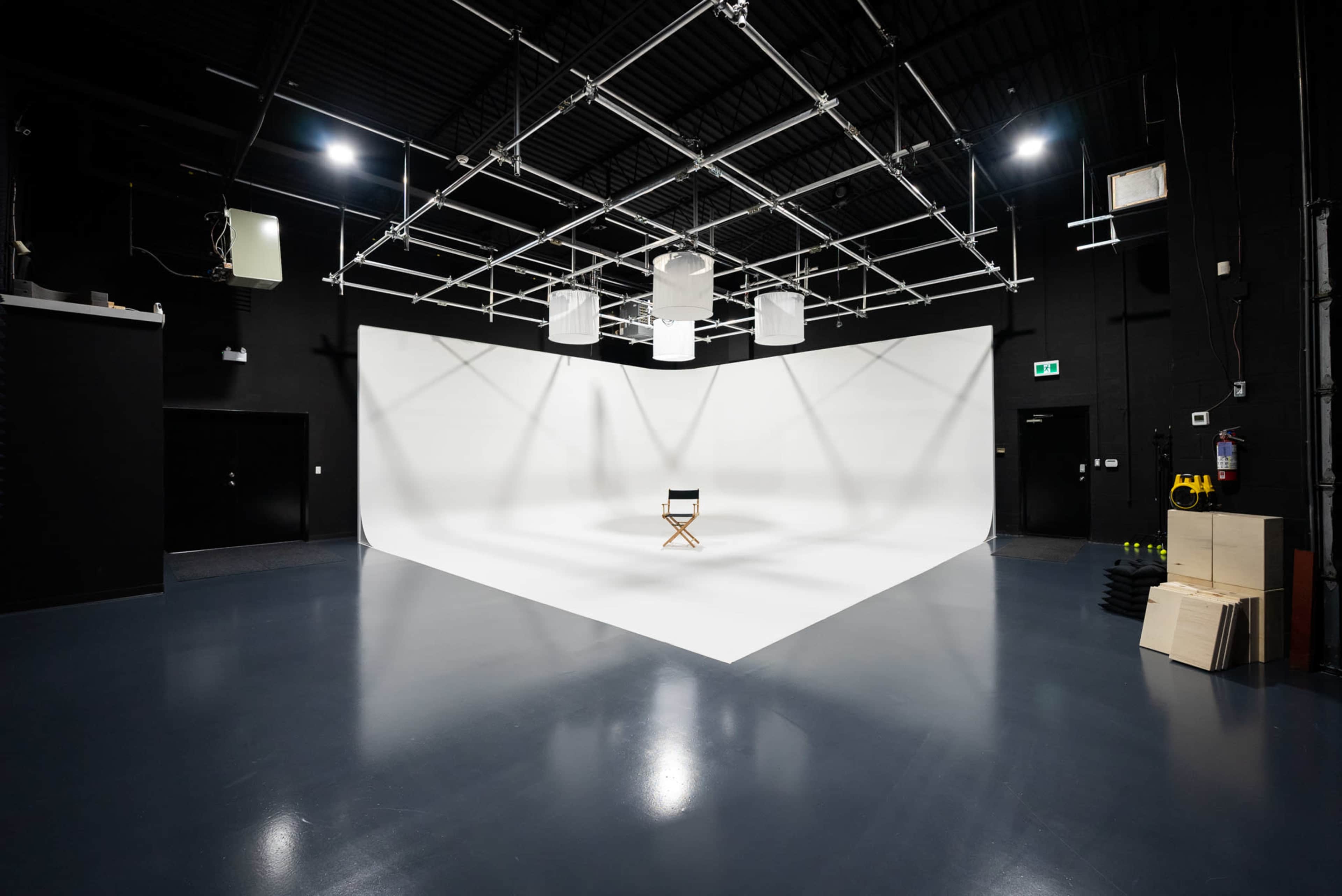 A film studio features a white backdrop with a single director's chair placed in the center.