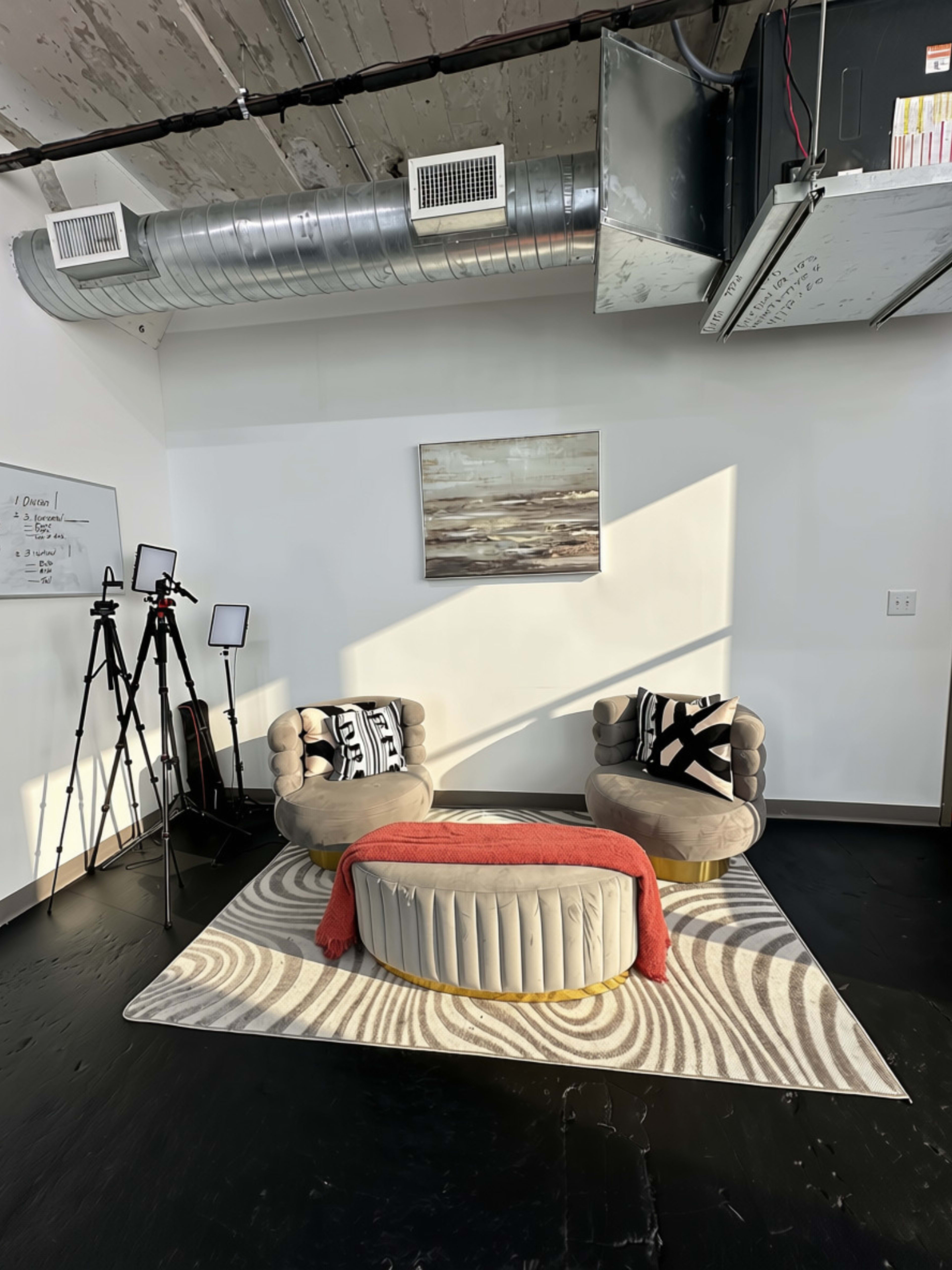 The image shows a modern interior space featuring two plush chairs and a round coffee table on a patterned rug, with studio lights positioned nearby.