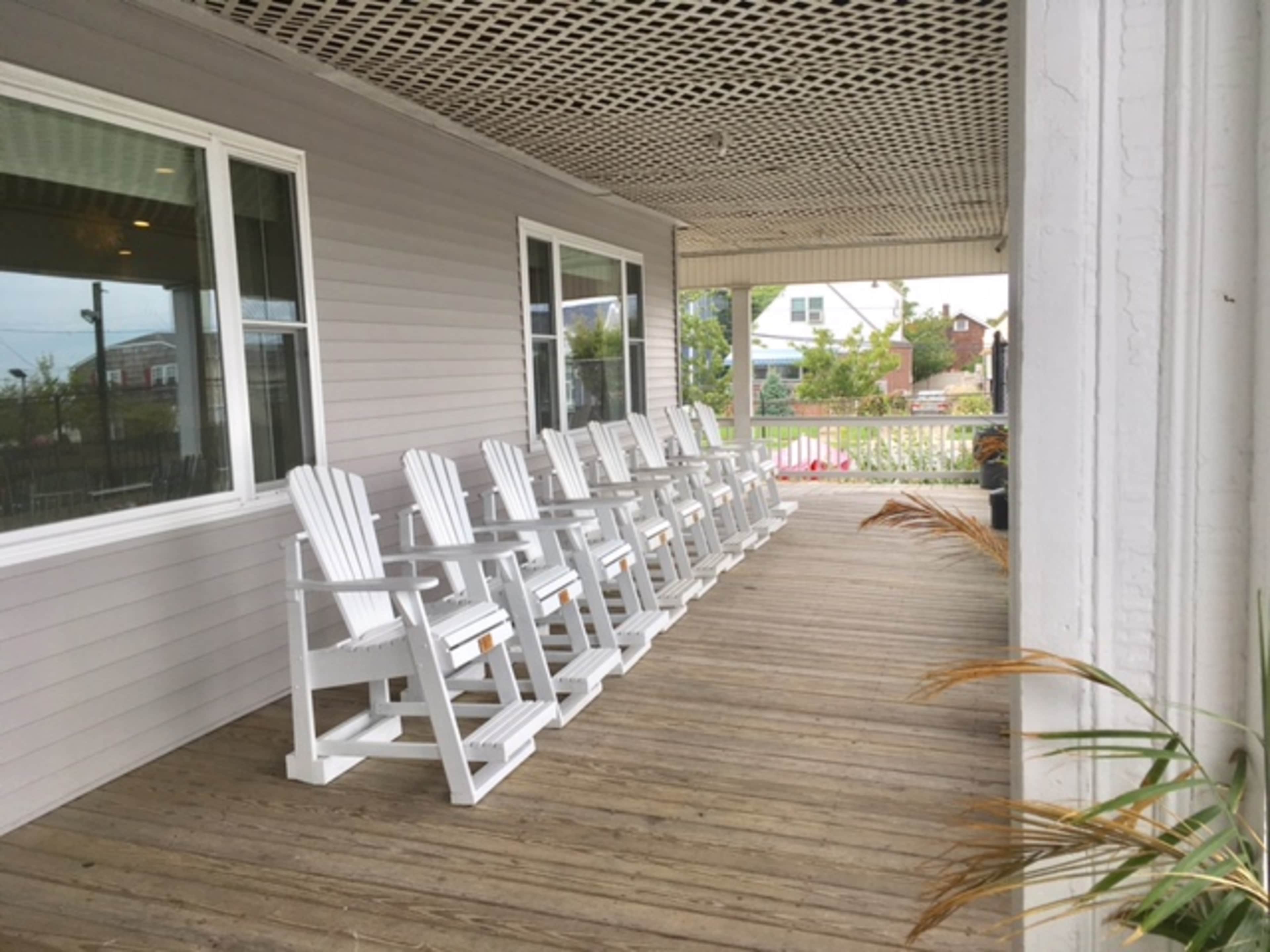 A row of white Adirondack chairs is lined up on a wooden porch with a slatted ceiling.