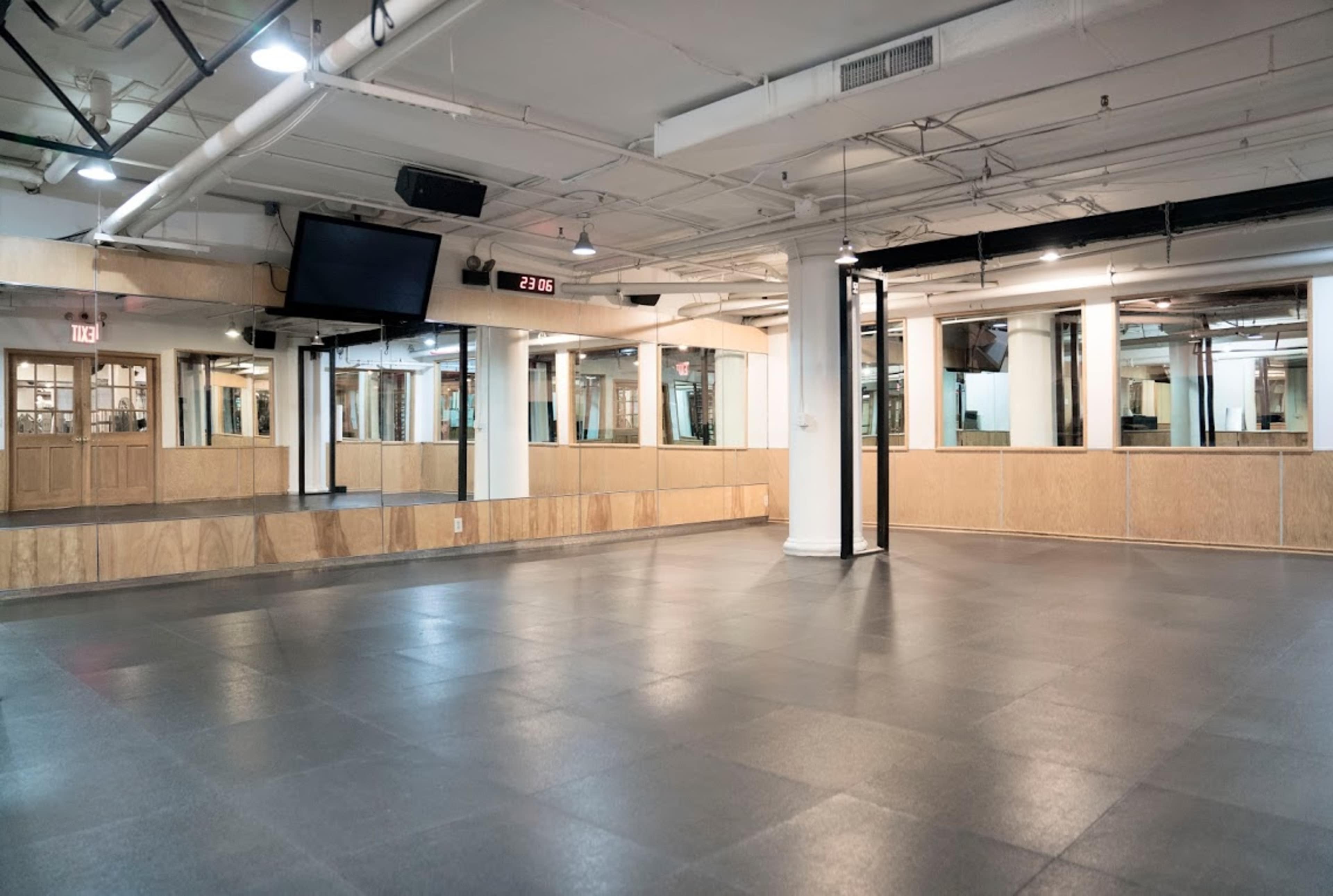 A large, empty indoor studio space with a smooth black floor, white columns, and mirrored walls, illuminated by overhead lighting.