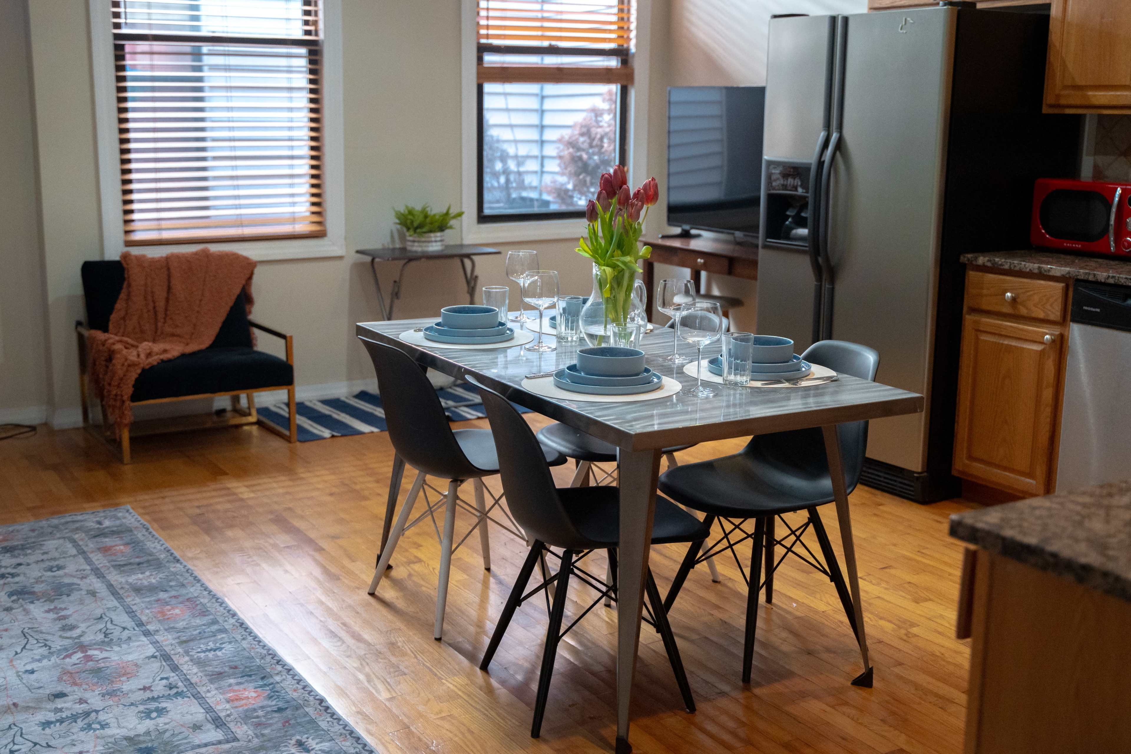 A dining table is set for a meal in a cozy kitchen, featuring a vase of tulips and modern black chairs.