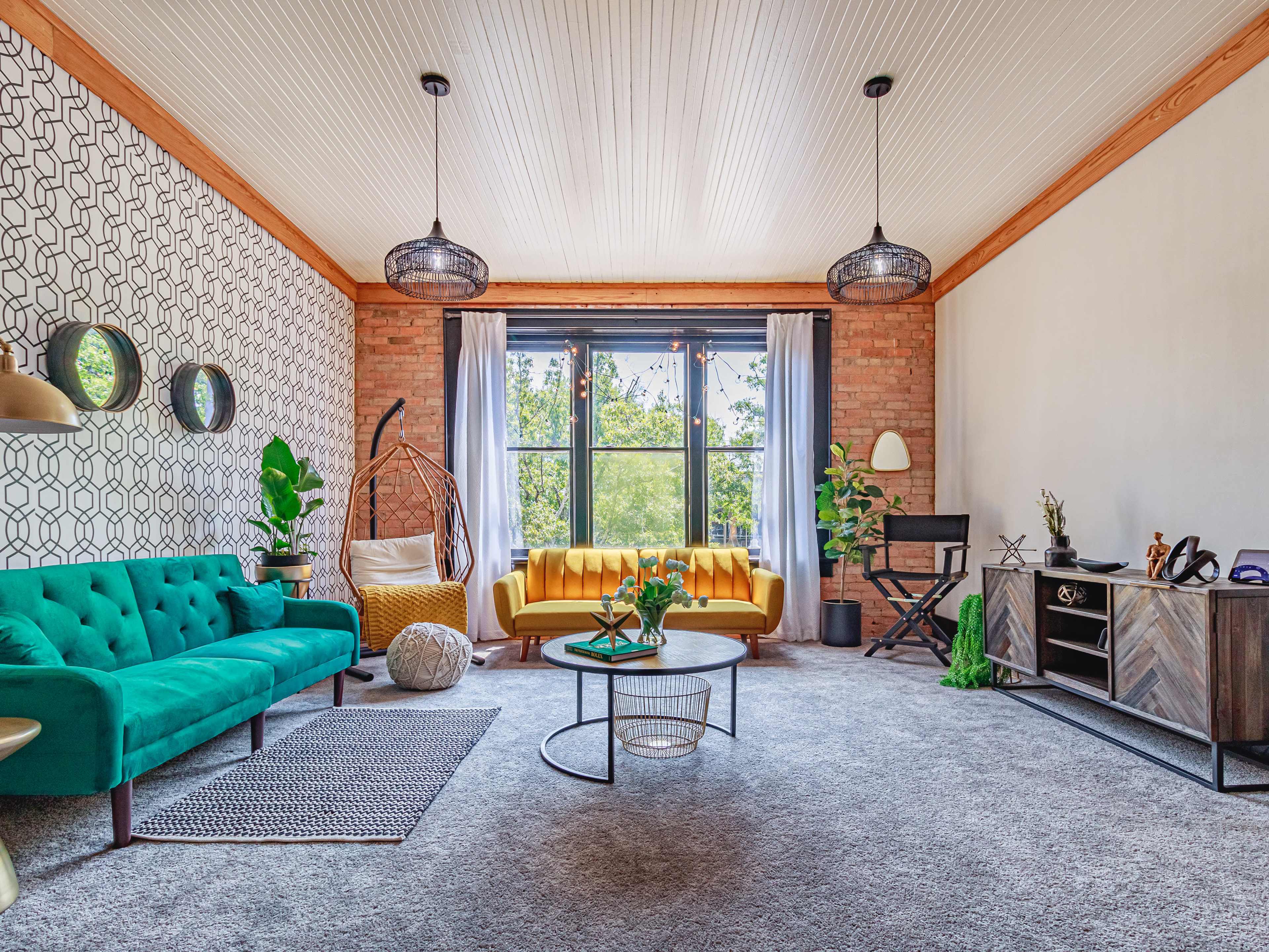 The image shows a stylish living room with a teal sofa, a yellow couch, a circular coffee table, and a mix of greenery and decorative elements.