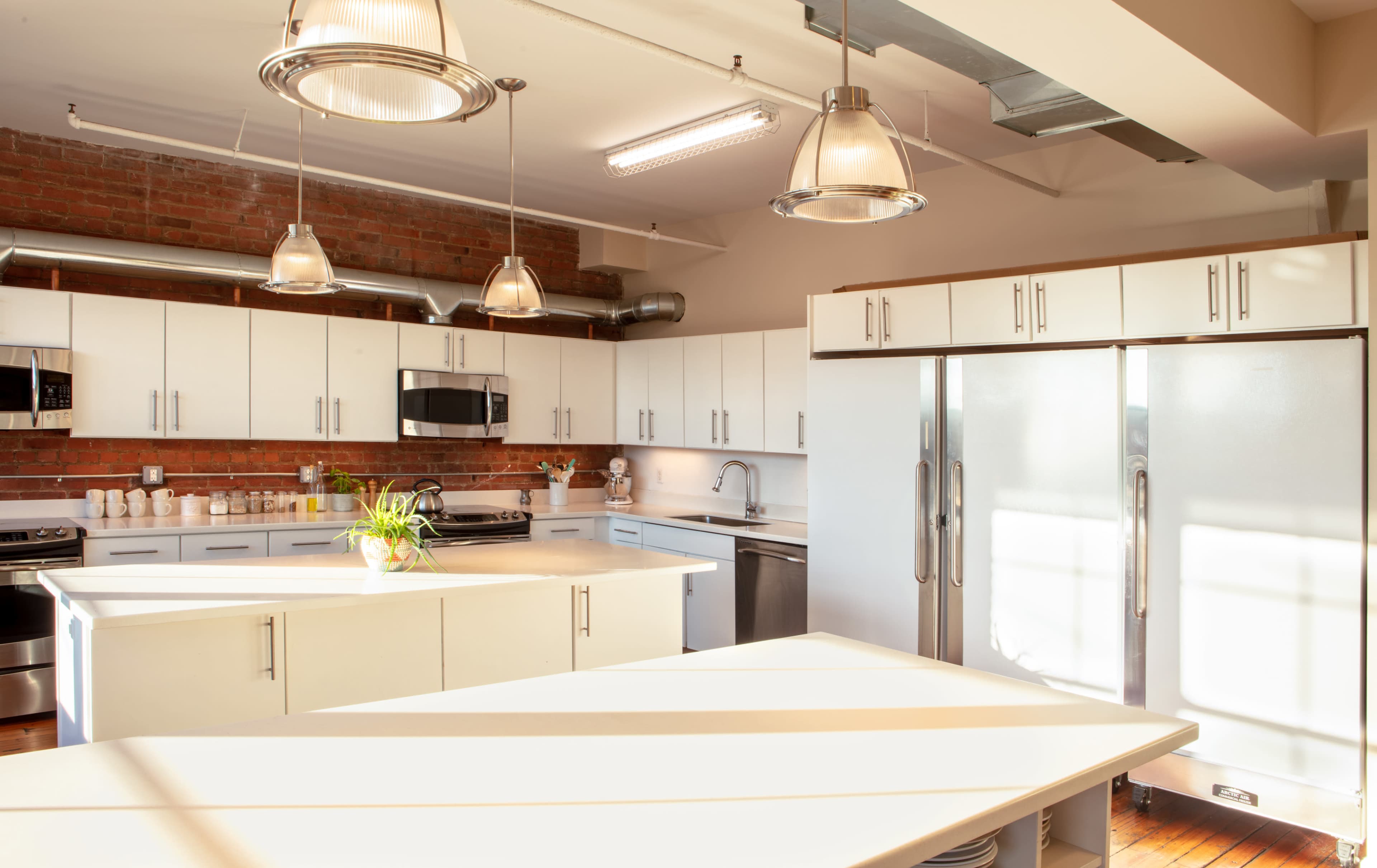 A modern kitchen with white cabinetry, stainless steel appliances, and a large island, illuminated by pendant lights.