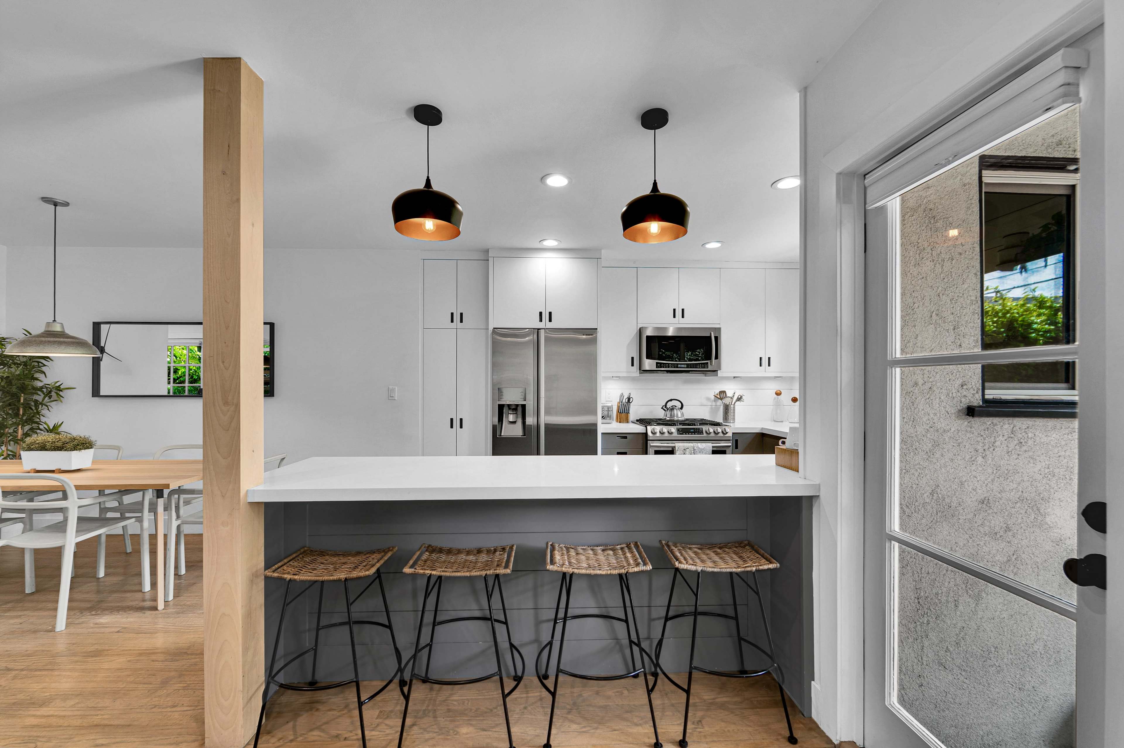 The image shows a modern kitchen with a white countertop, four bar stools, and stainless steel appliances.