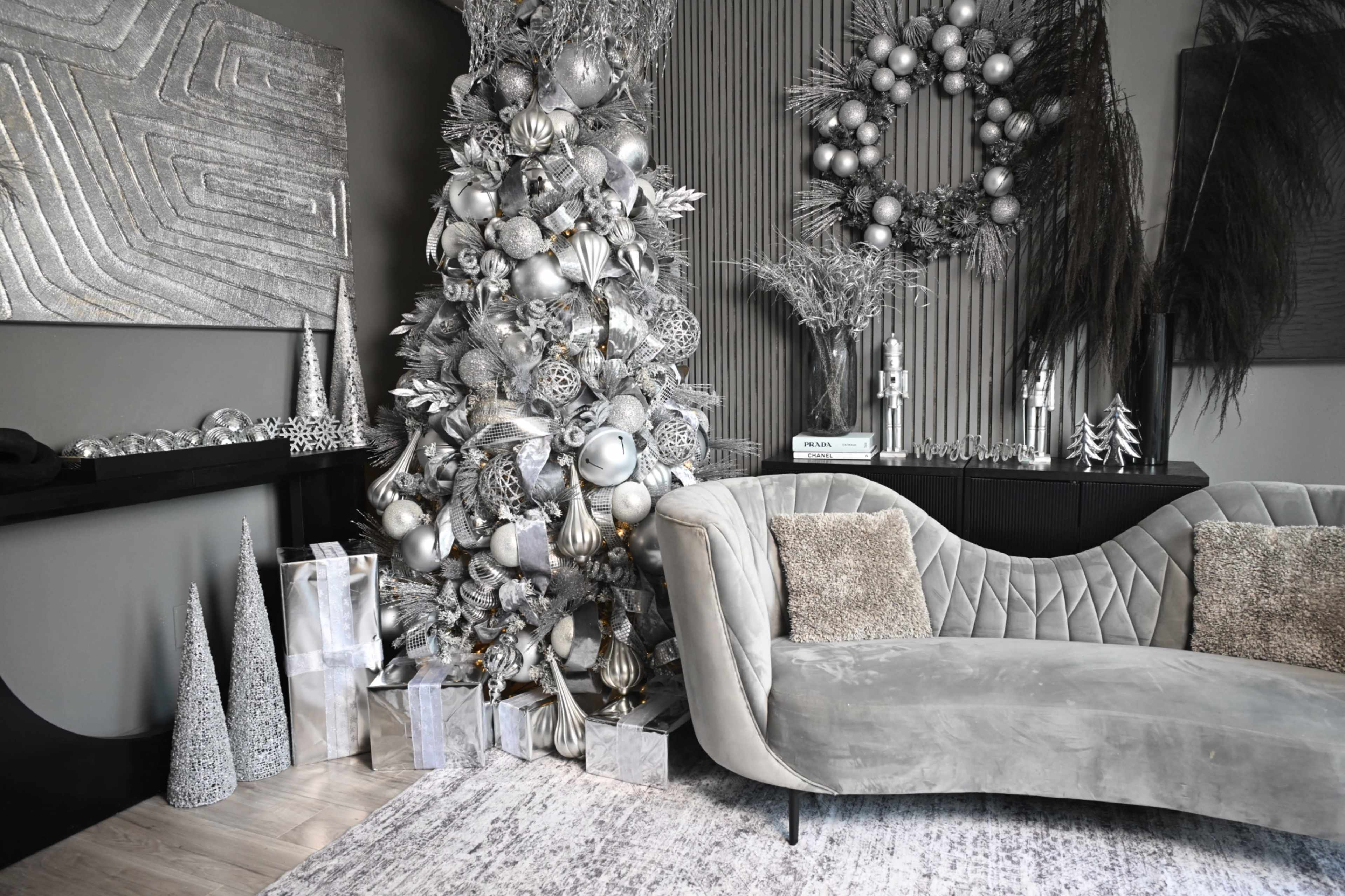 The scene features a stylish living room decorated with a silver and white Christmas tree, elegant ornaments, and contemporary furnishings, including a plush sofa and decorative accents.