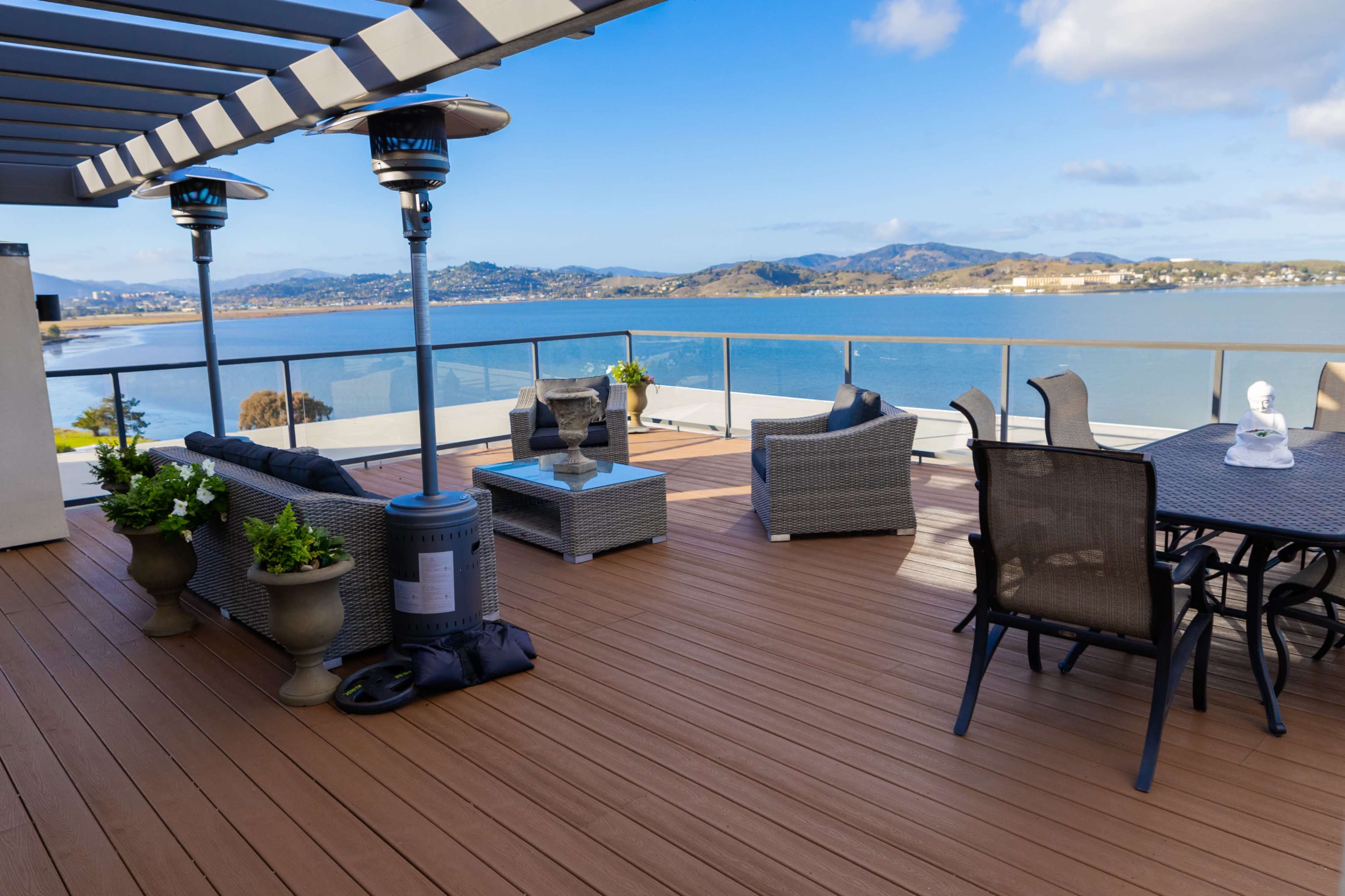 A spacious outdoor terrace features modern seating arrangements, decorative plants, and a scenic view of the water and mountains.