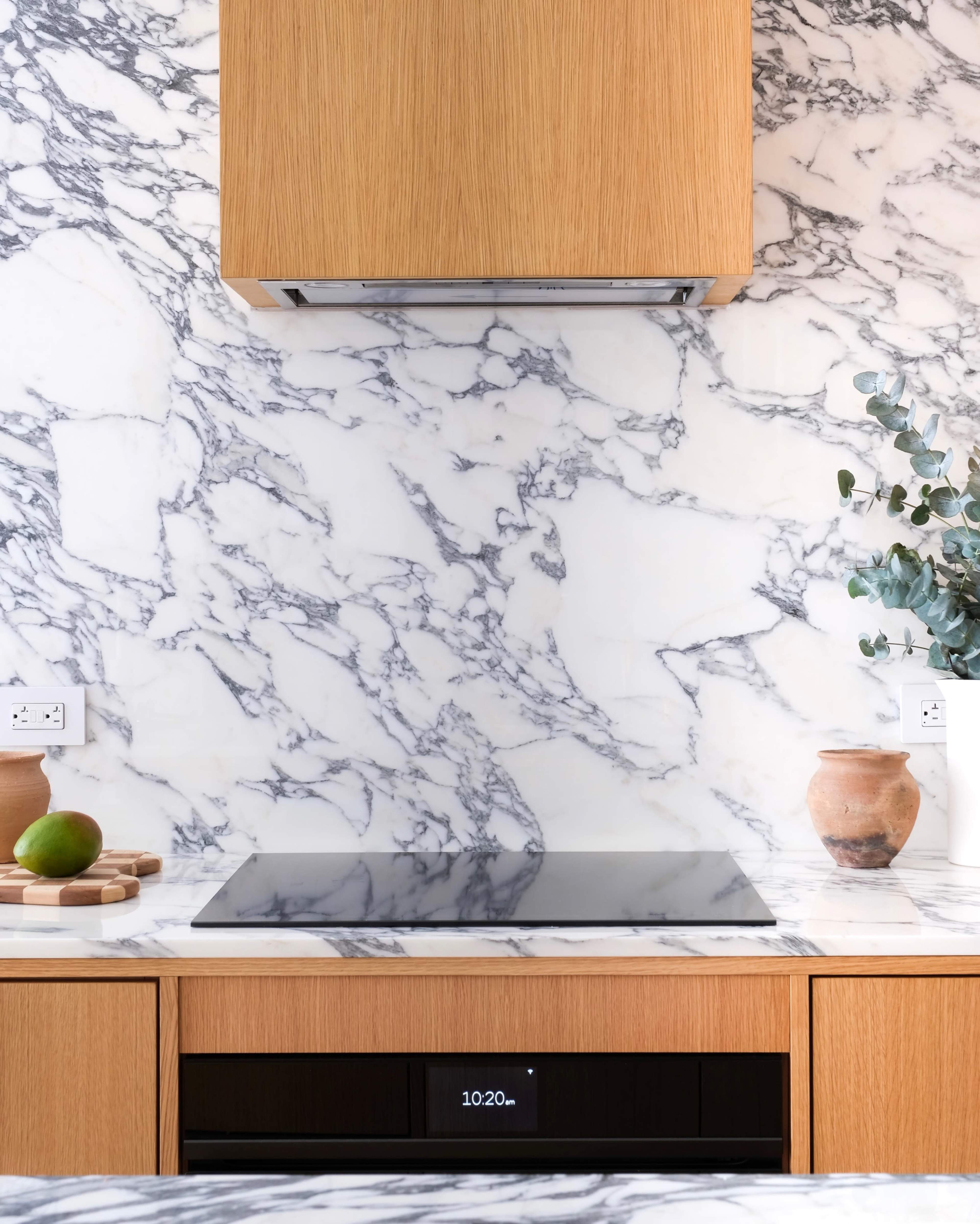 A modern kitchen features a marble backsplash, a black stovetop, and wooden cabinetry.