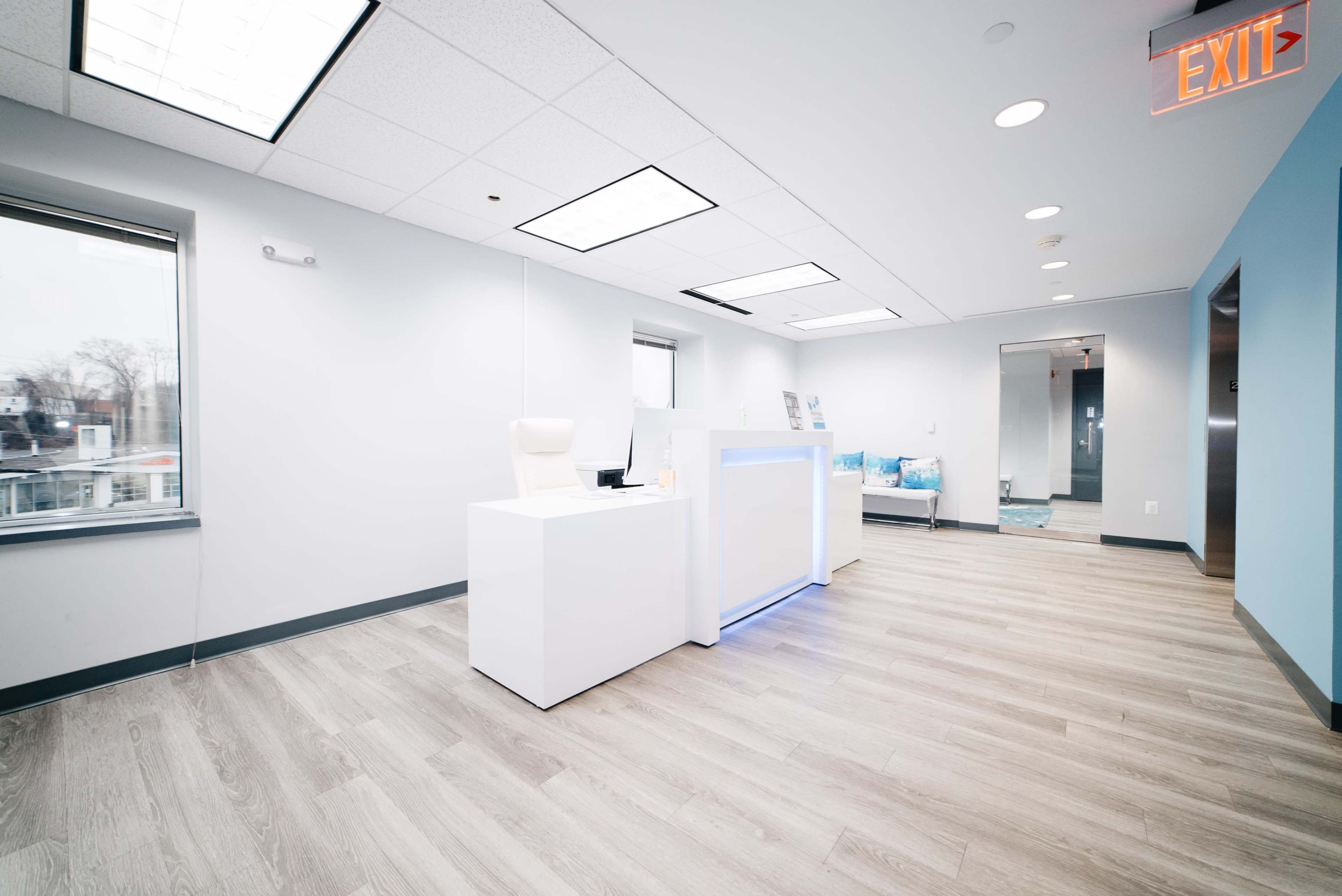 A modern, uncluttered office reception area with a white desk and light wood flooring.