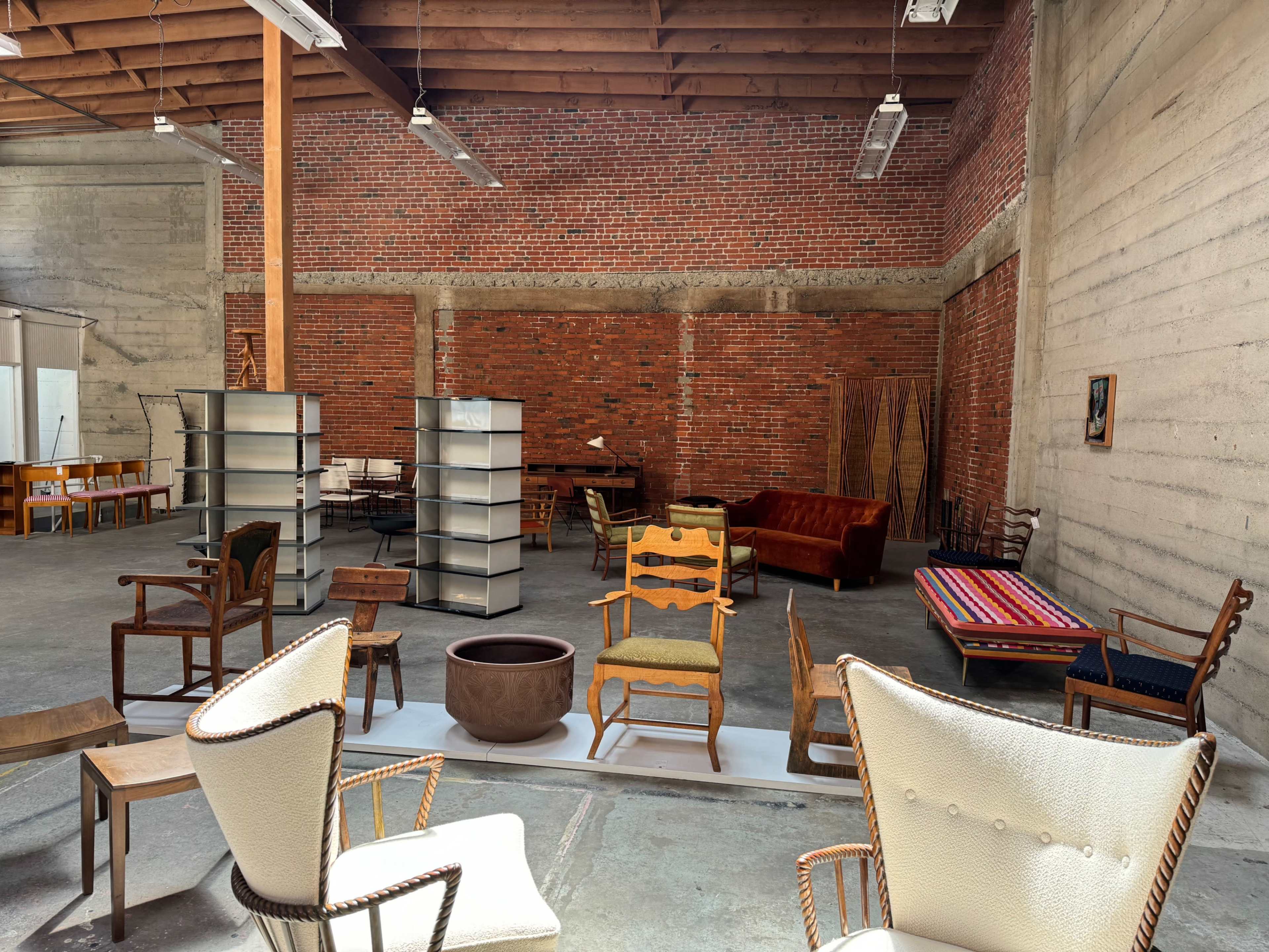 A spacious interior filled with various styles of furniture, including chairs and tables, against a backdrop of exposed brick and concrete walls.