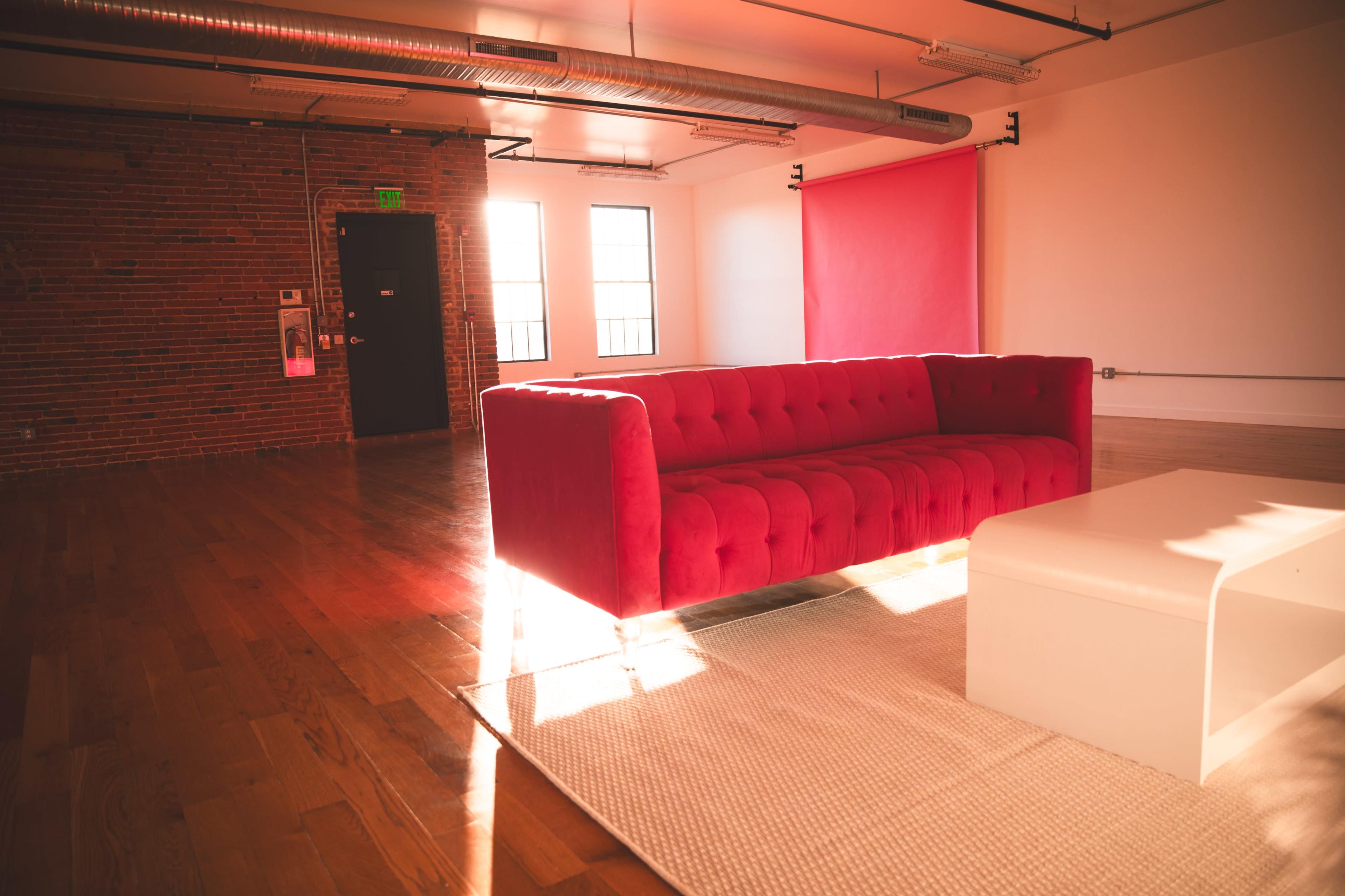 The image shows a bright room with a red tufted couch, a white coffee table, and a large window allowing natural light to fill the space.
