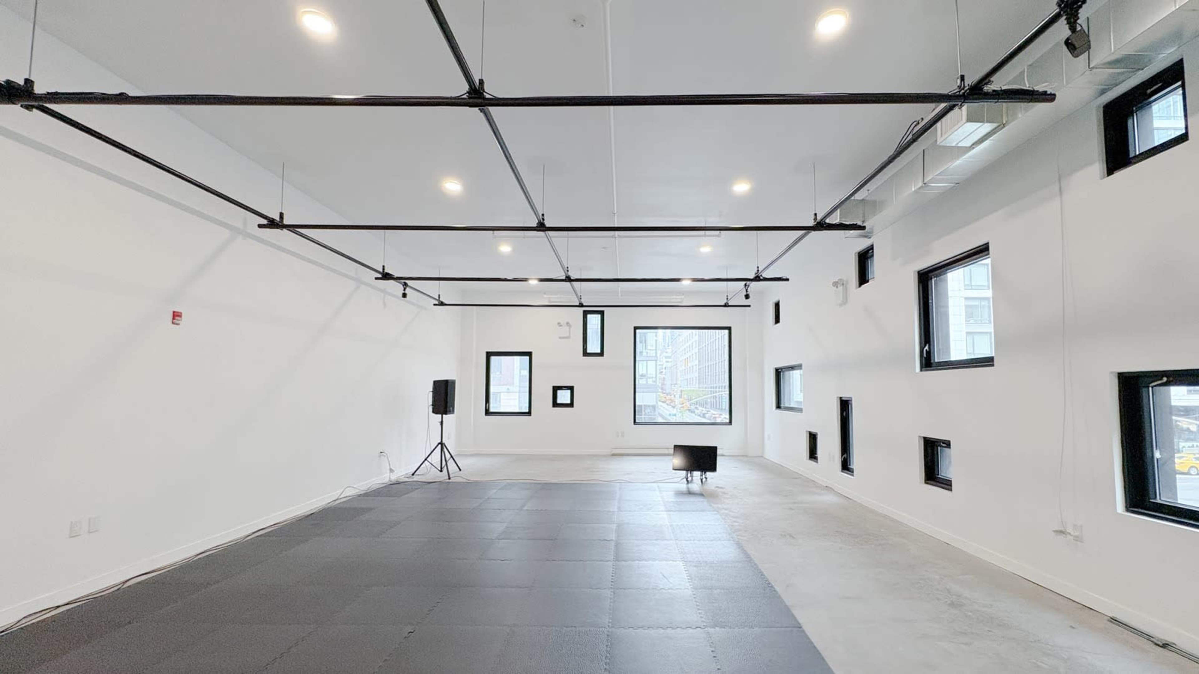 The image shows a spacious, modern interior with large windows, white walls, and a black floor mat area.