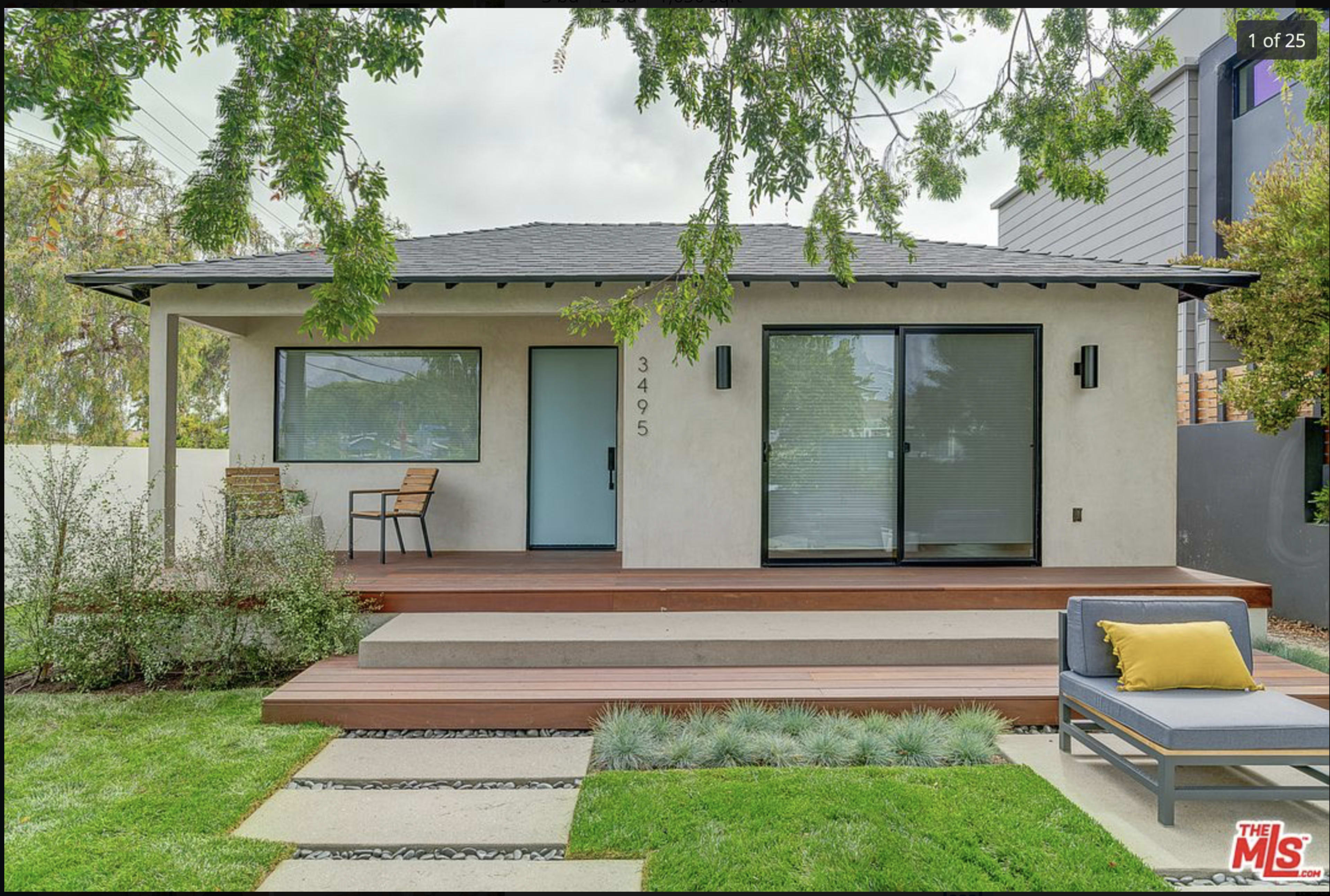 A modern single-story house with a front porch, wooden steps, and a landscaped yard featuring grass and shrubs.